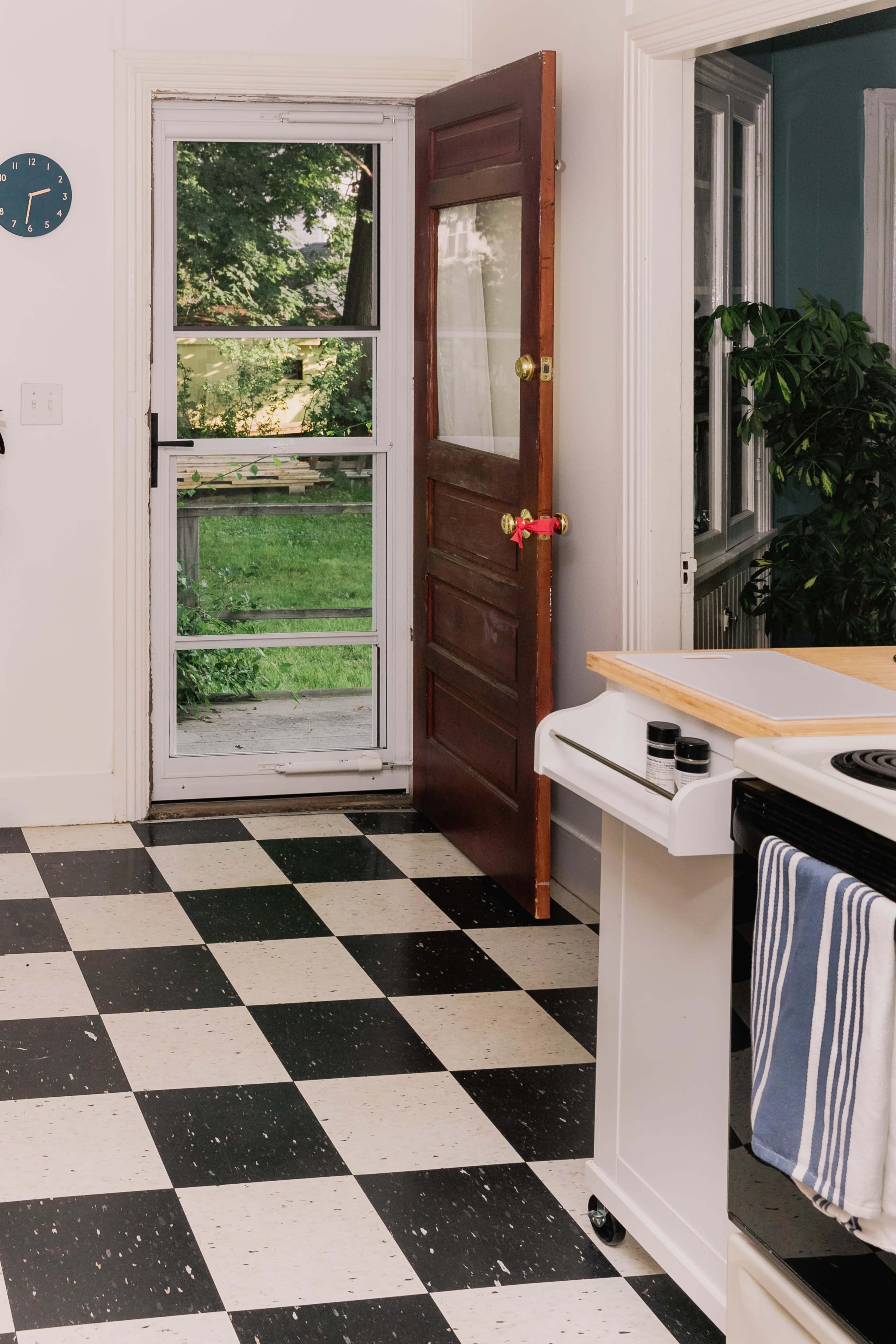 A kitchen with black and white checkered flooring features an open door leading to a green backyard.