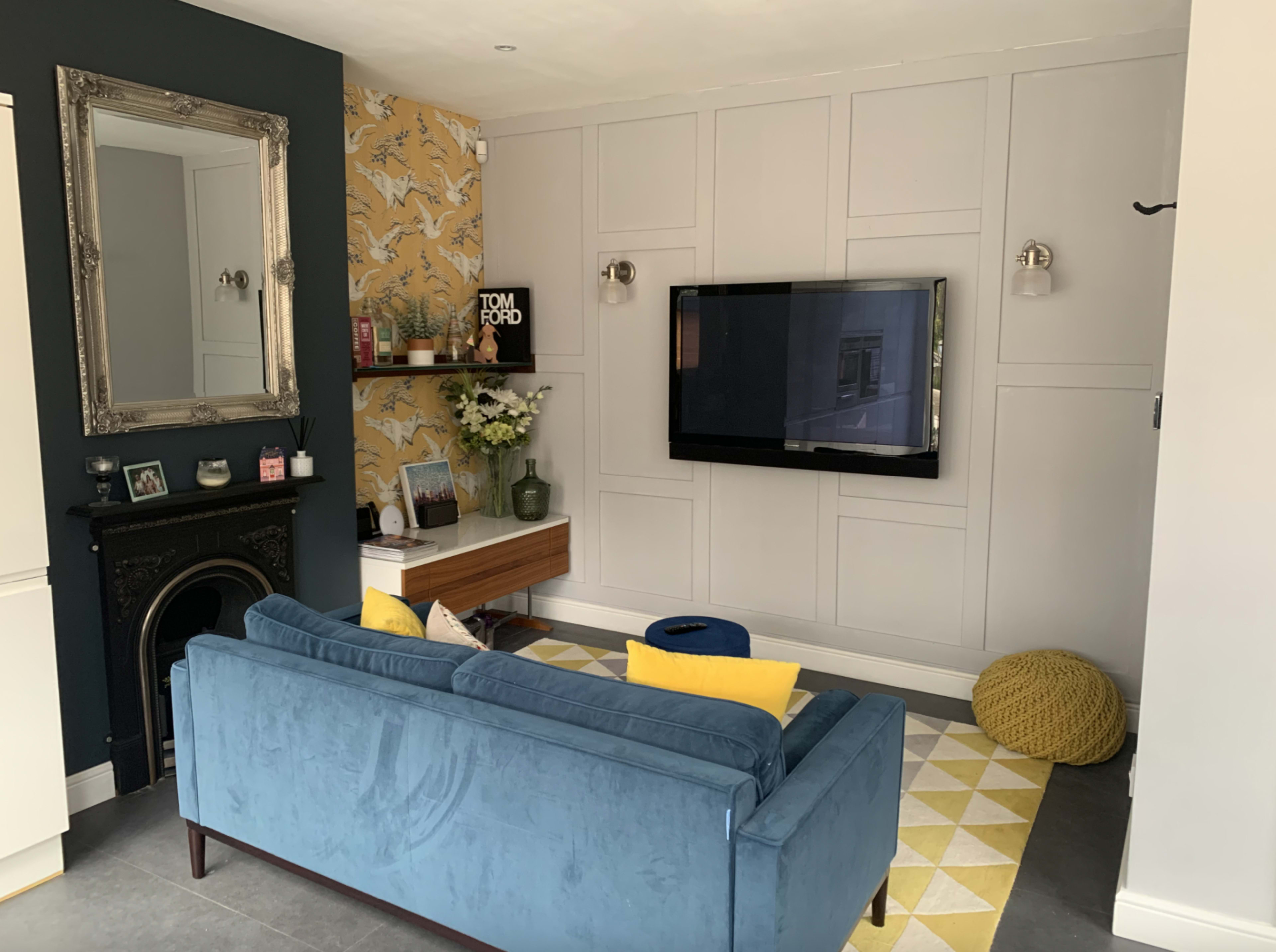 The living room features a blue velvet sofa facing a mounted television, with decorative walls and a blend of modern and vintage furnishings.