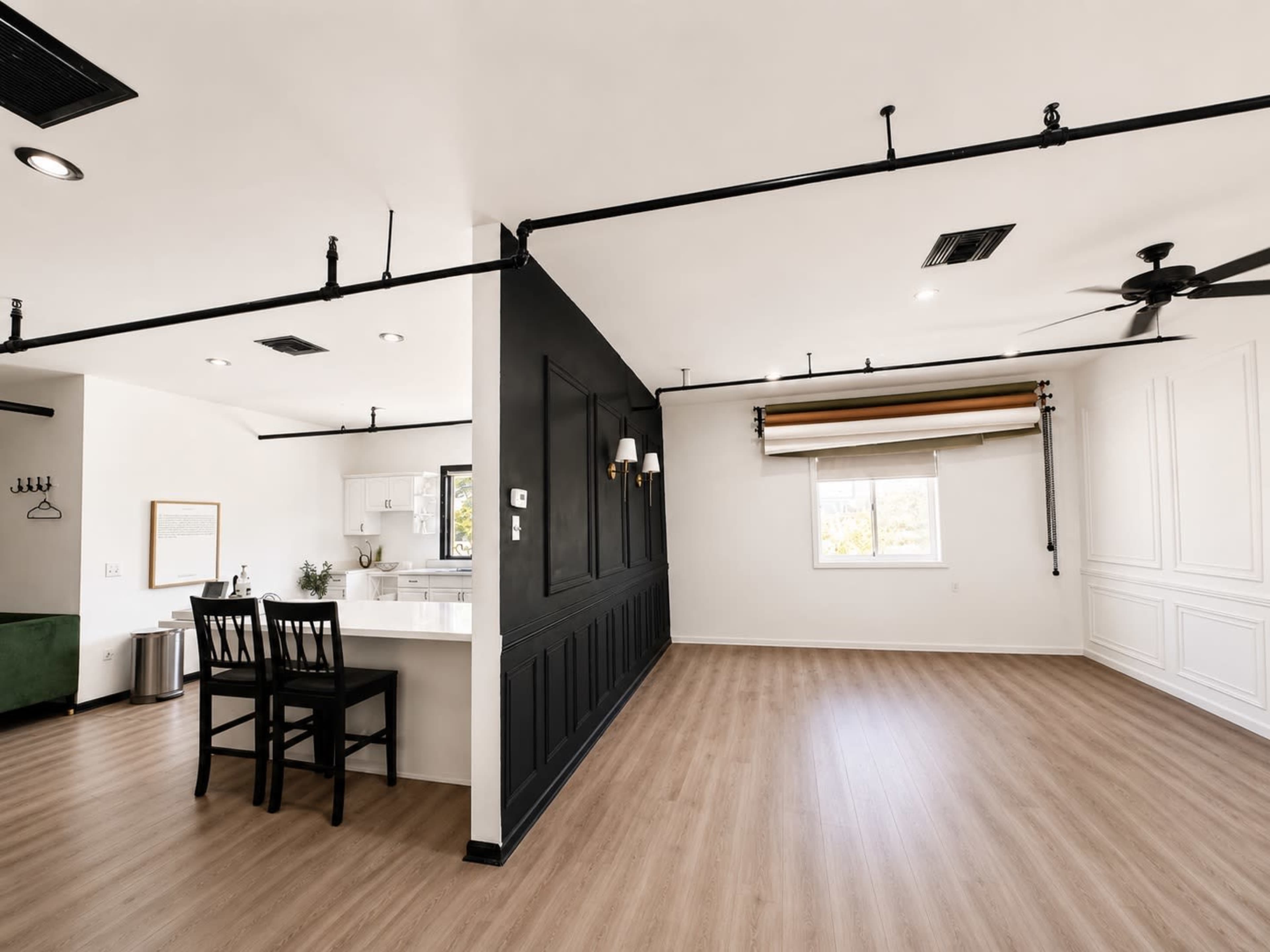 The image shows a spacious, modern interior with a kitchen area on the left and a large open space with wood flooring and minimal furnishings in the foreground.