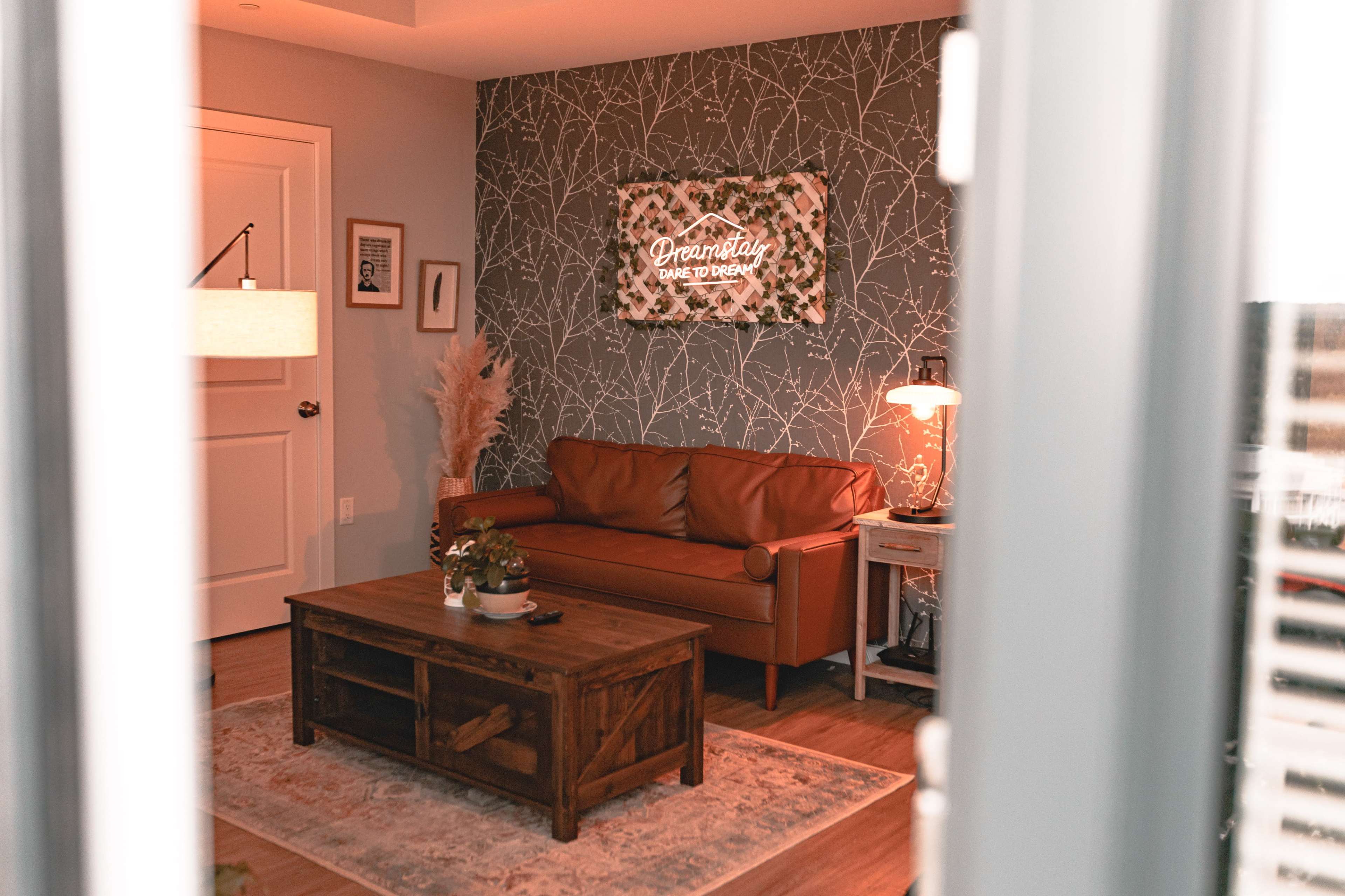 A cozy living room features a brown leather sofa, a wooden coffee table, and a decorative wall with a neon sign above it.