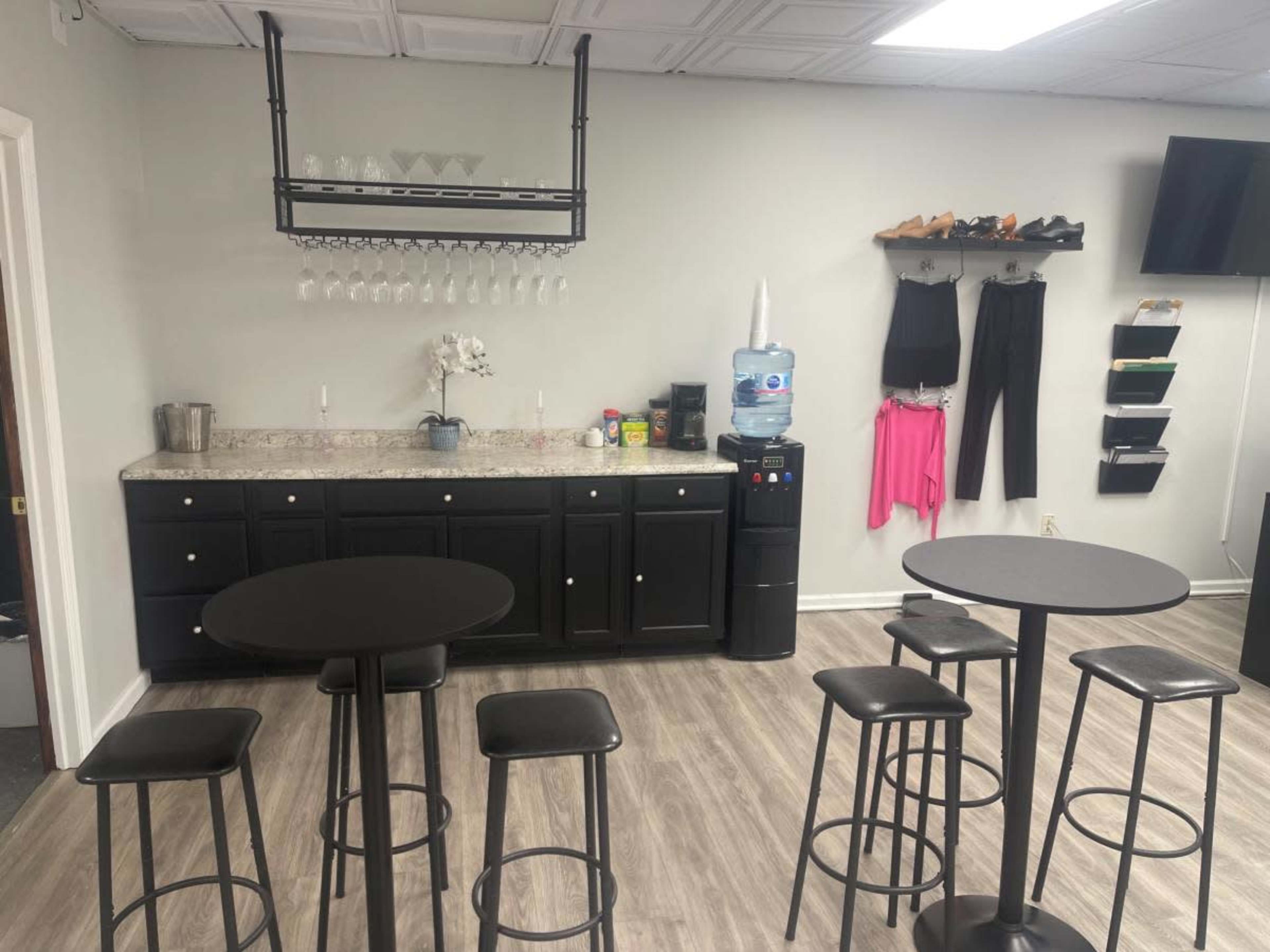 A modern break room with a granite countertop, a water cooler, and several tall black tables and stools.