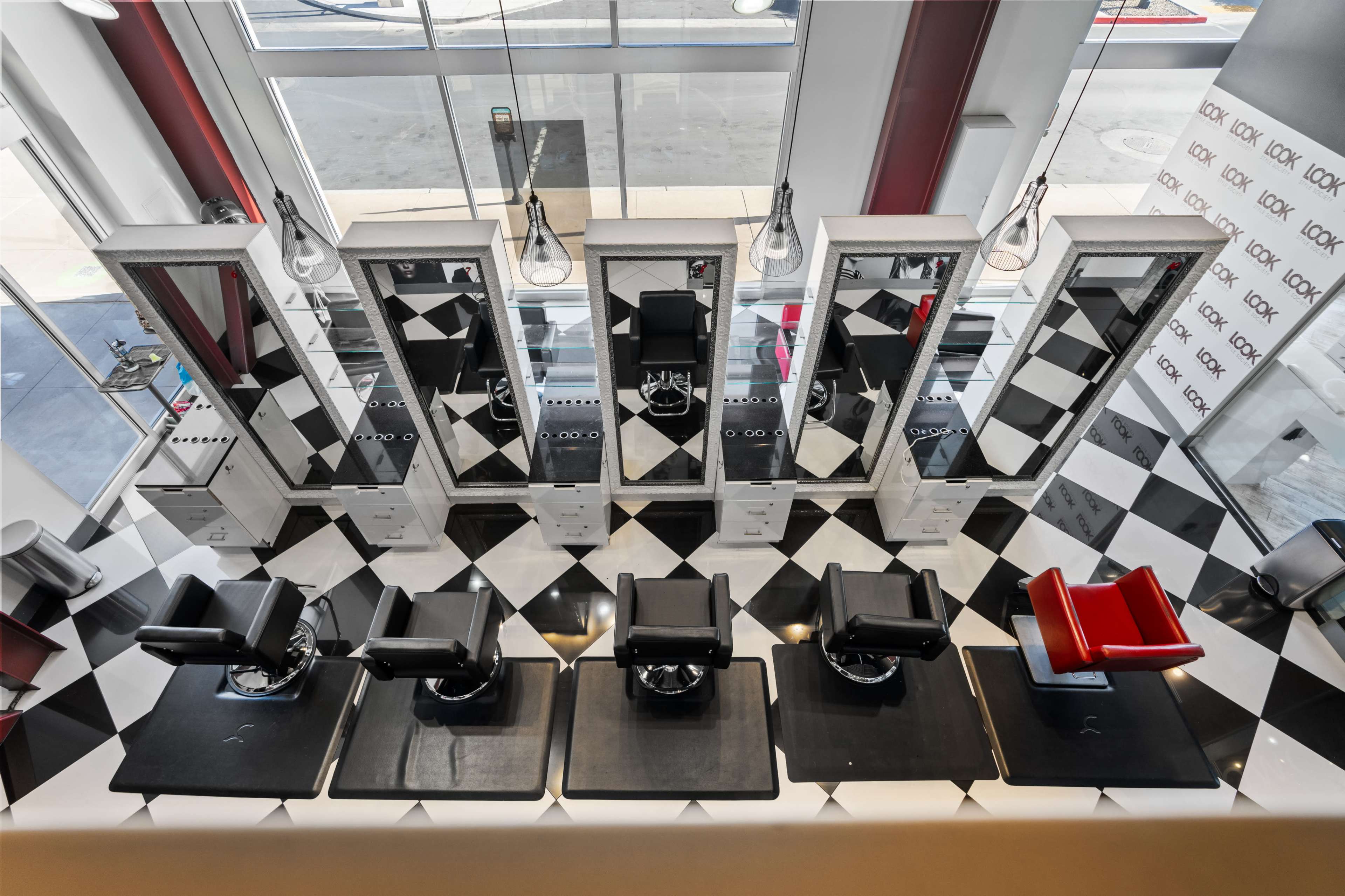 An aerial view of a barber shop with six black barber chairs arranged in front of mirrors on a checkered floor.