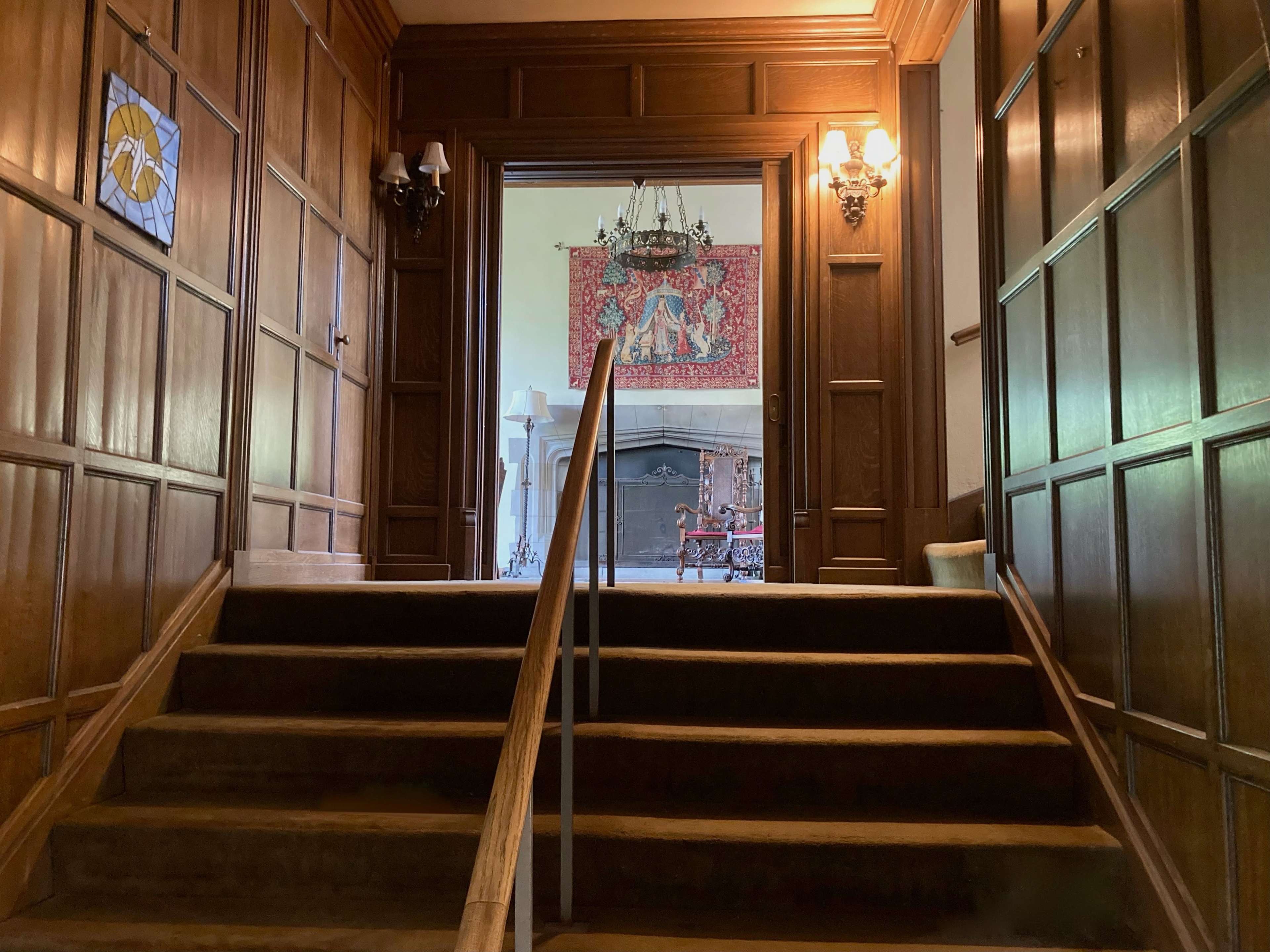 A beautifully crafted wooden staircase leading to an open doorway, with ornate wall sconces lighting the path.