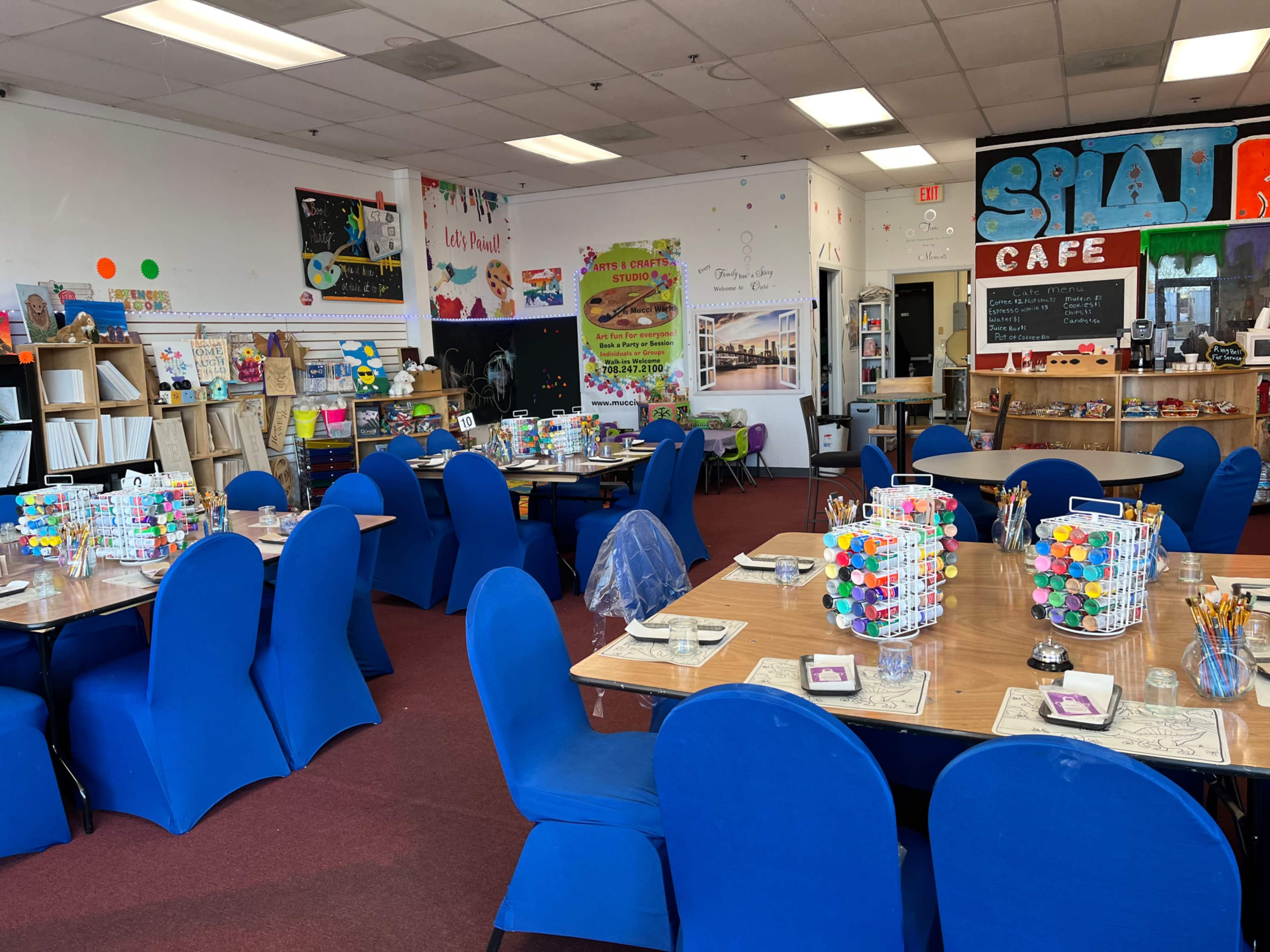 A brightly decorated art studio with blue chairs arranged around tables, each set with art supplies and colorful materials.
