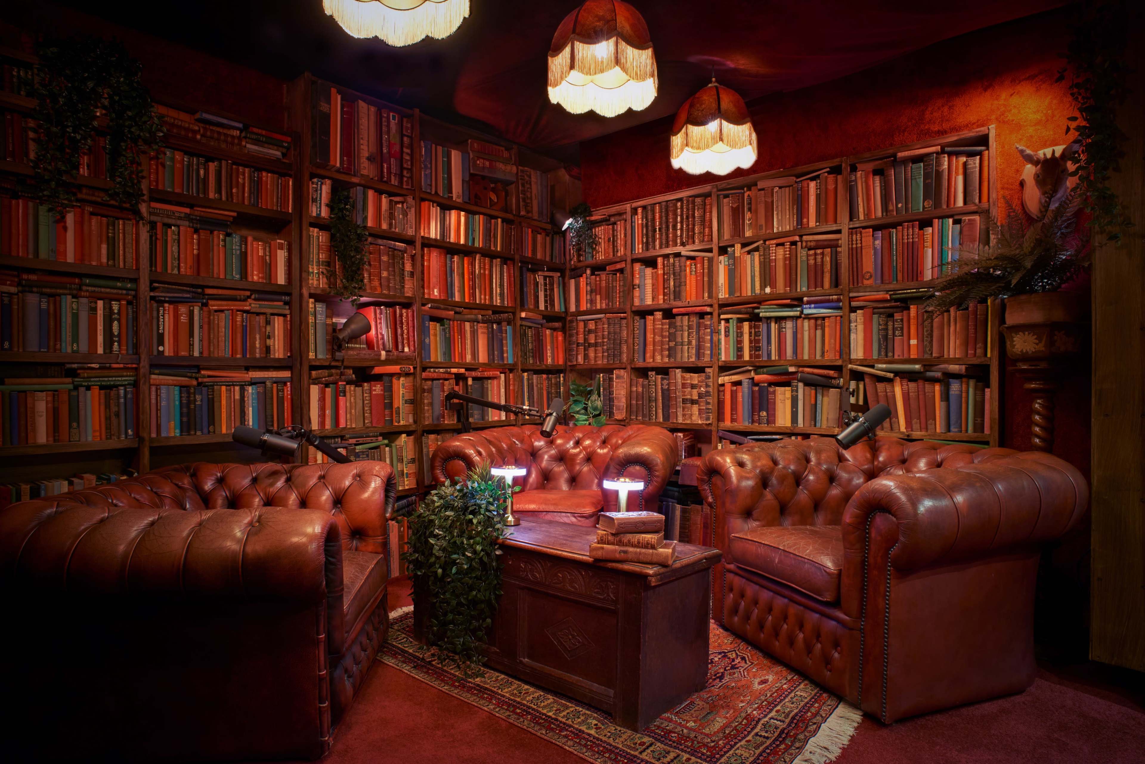 A cozy reading nook features two leather chesterfield sofas, a wooden coffee table, and bookshelves filled with neatly arranged books.
