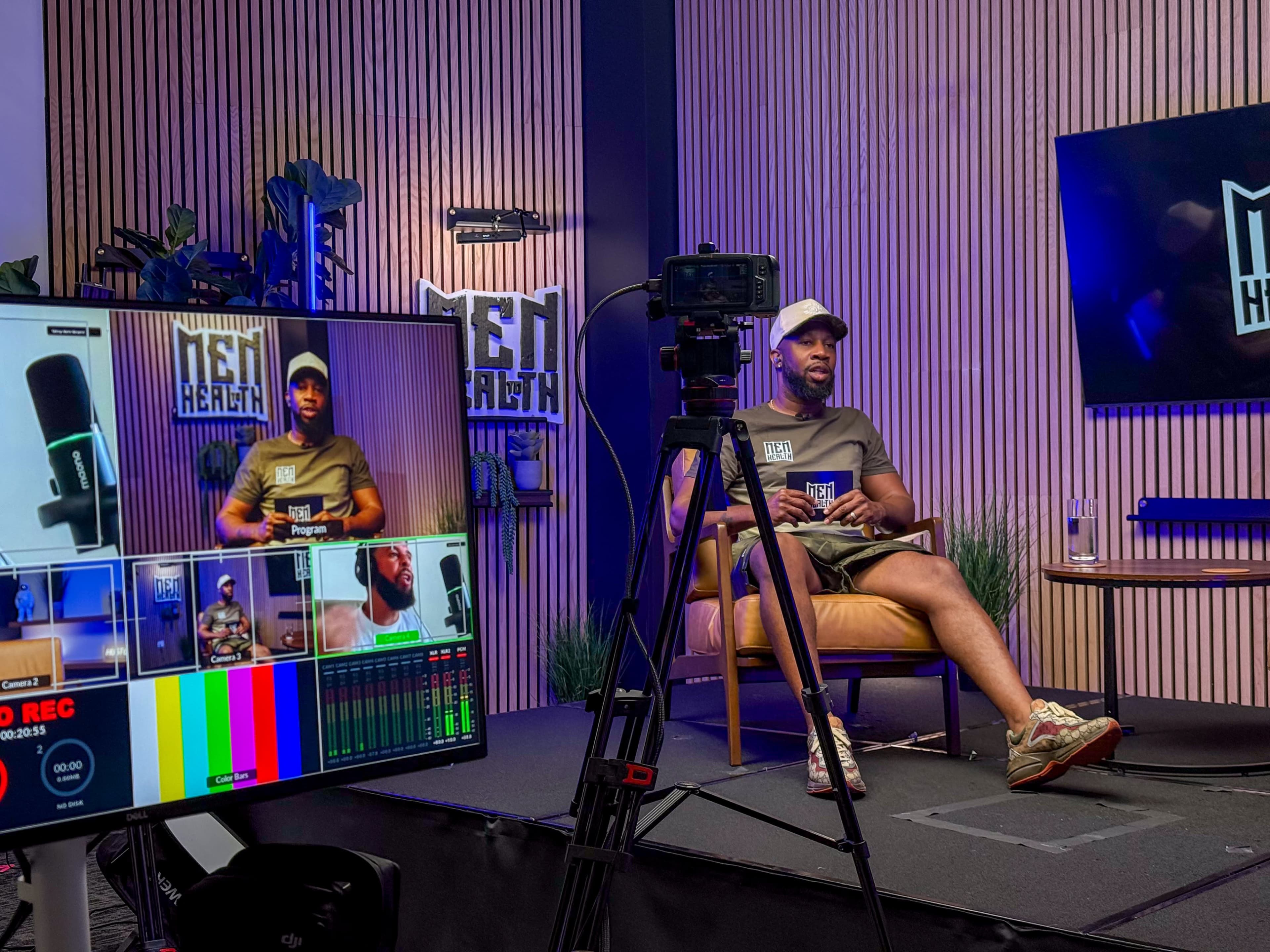 A man sits in a studio setting equipped with cameras and screens, discussing topics related to men's health.