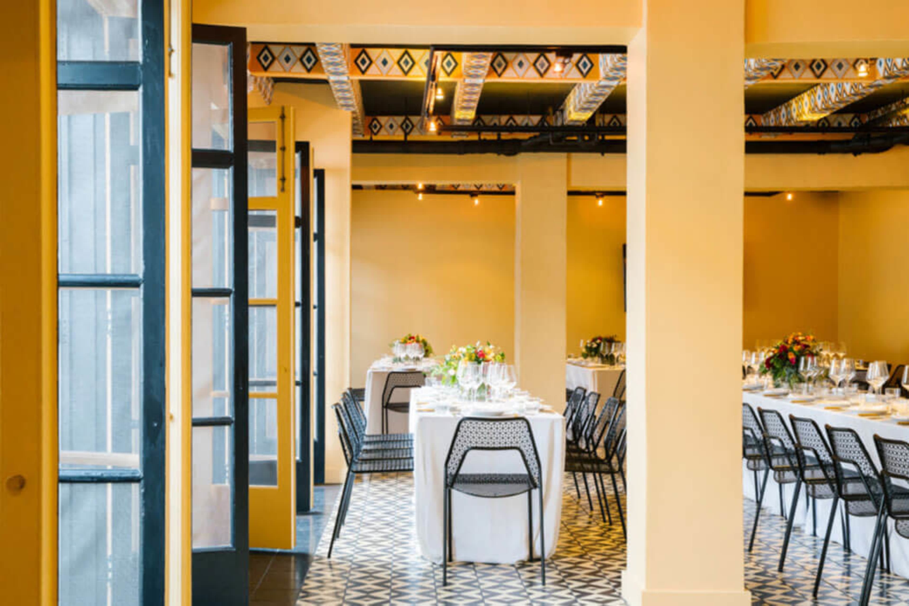 The image shows an elegantly set dining room with tables arranged for a formal meal, featuring yellow walls and patterned flooring.