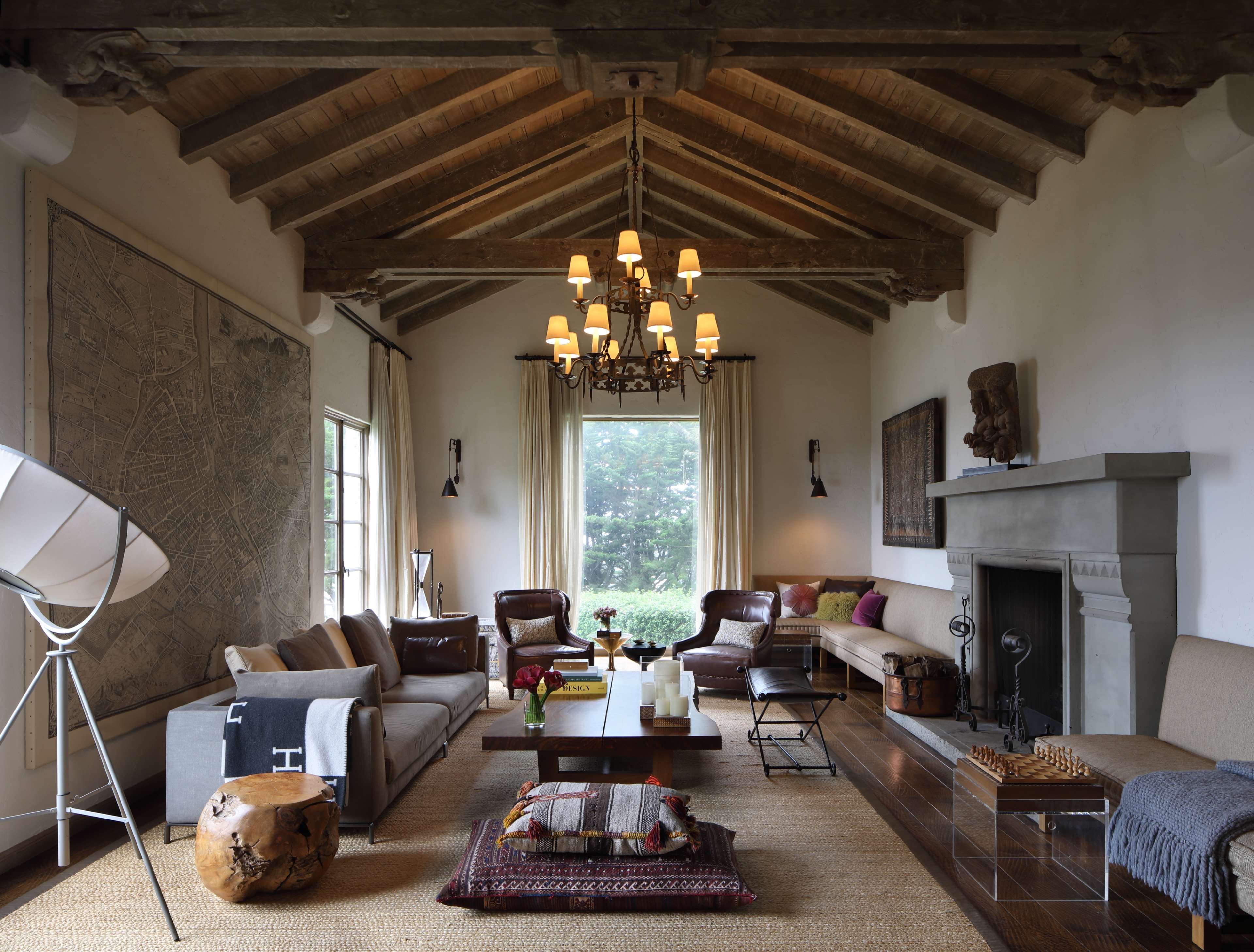 The living room features a high-beamed ceiling, a fireplace, and a mix of modern and rustic furnishings arranged around a central coffee table.