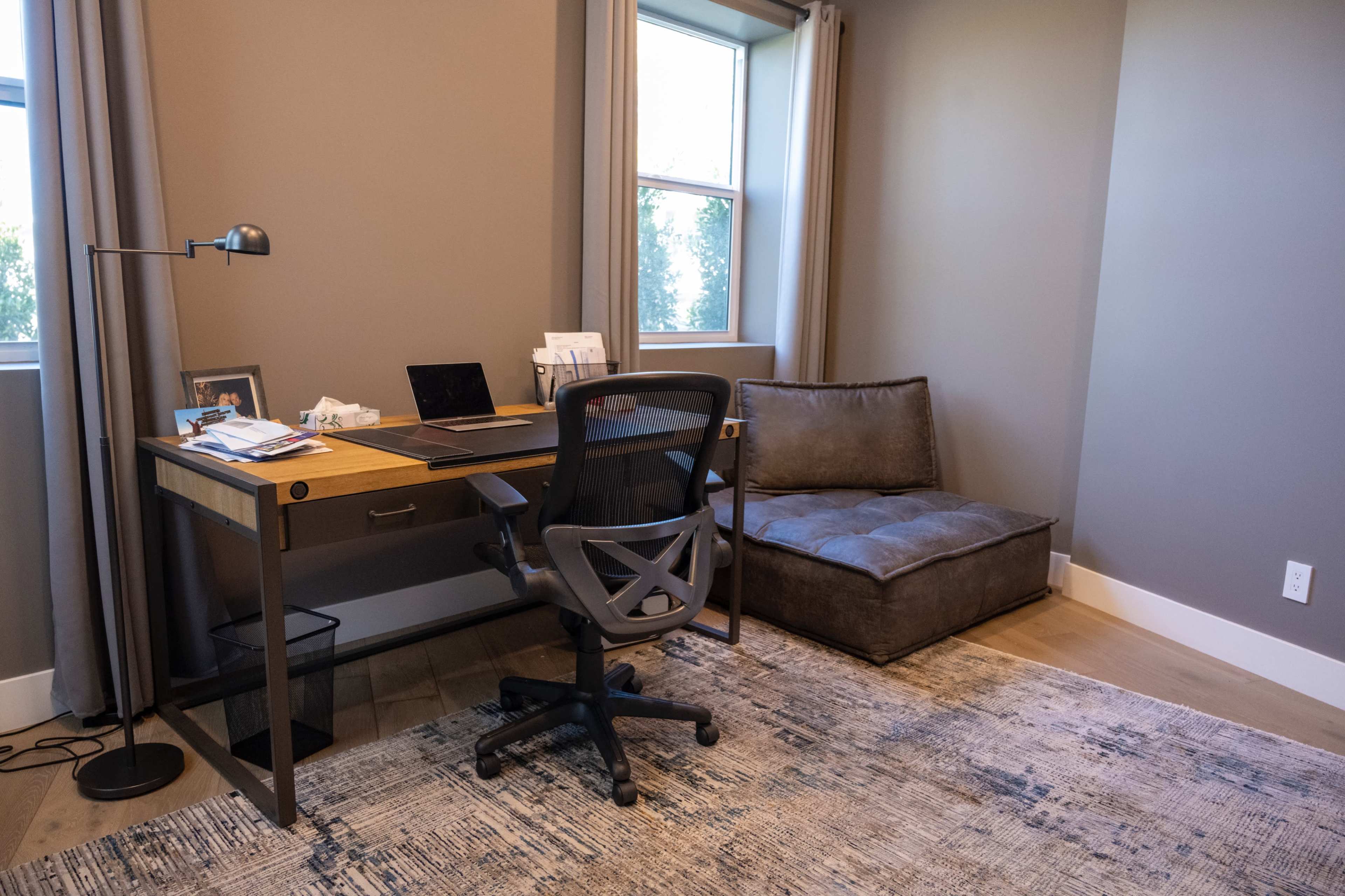 A modern home office with a desk, chair, and a seating area beside a window.