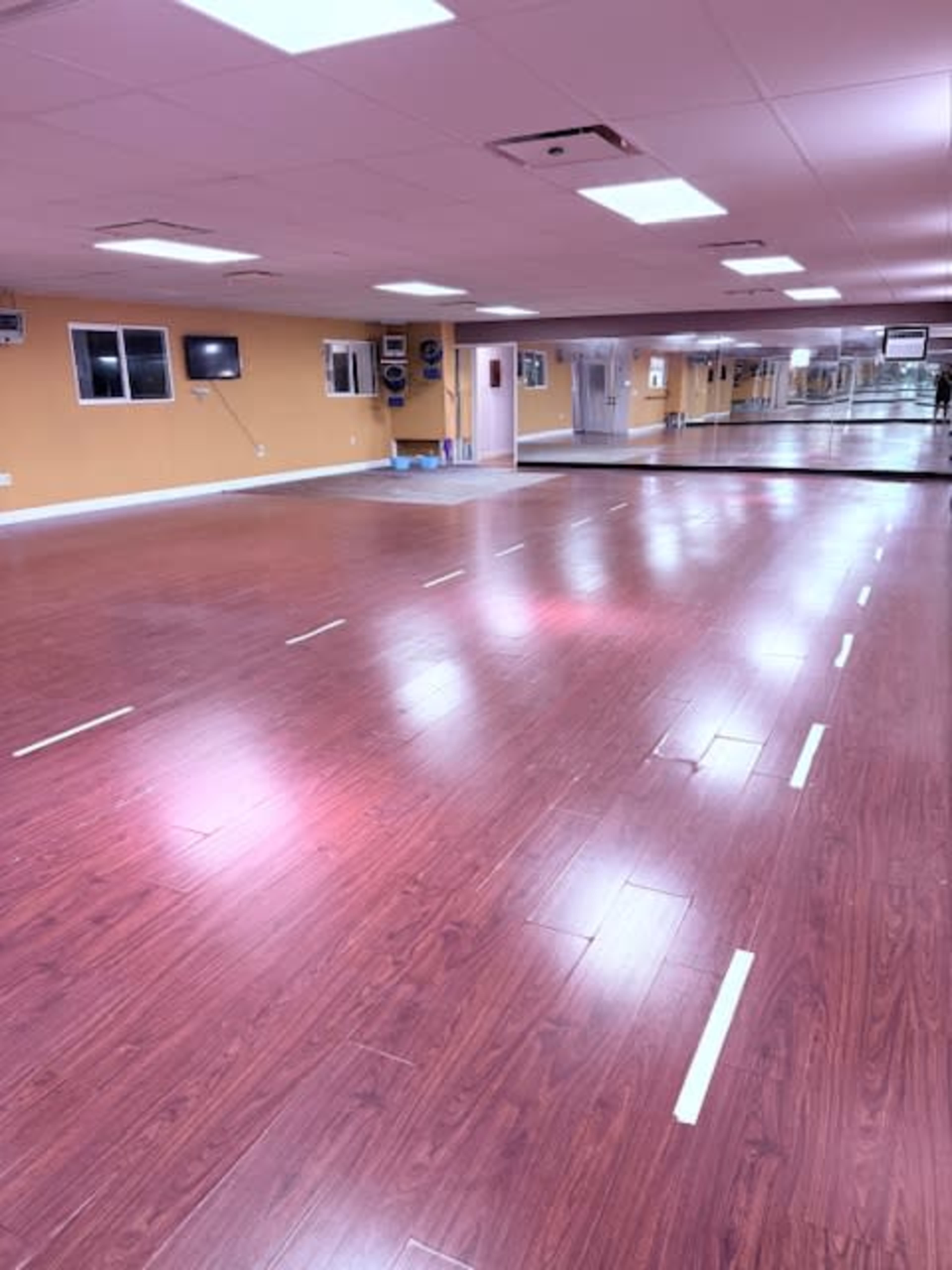The image shows an empty studio space with wooden flooring, mirrors on one wall, and yellow walls.