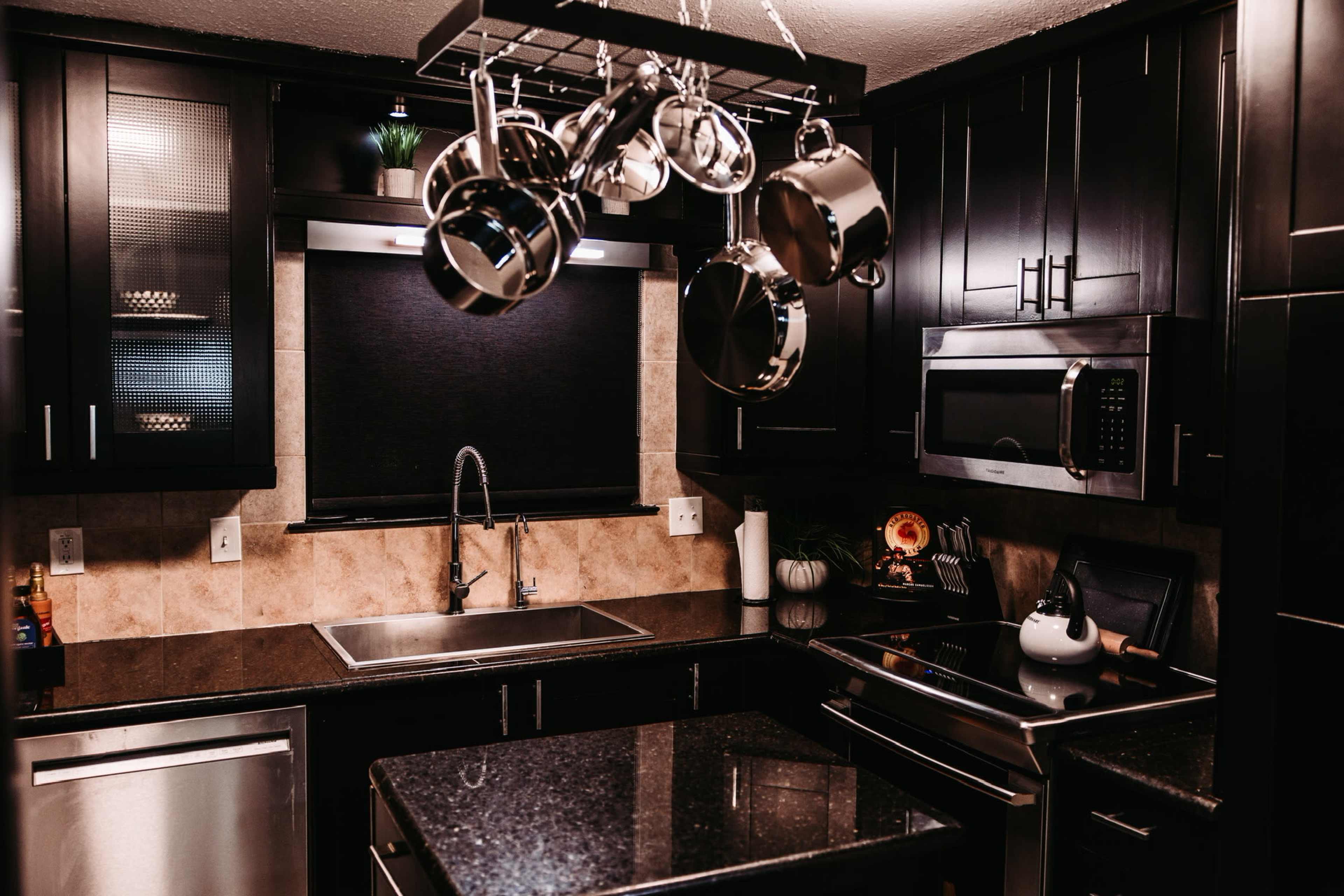 A modern kitchen with dark cabinetry, a stainless steel sink, and a pot rack hanging above a central island.