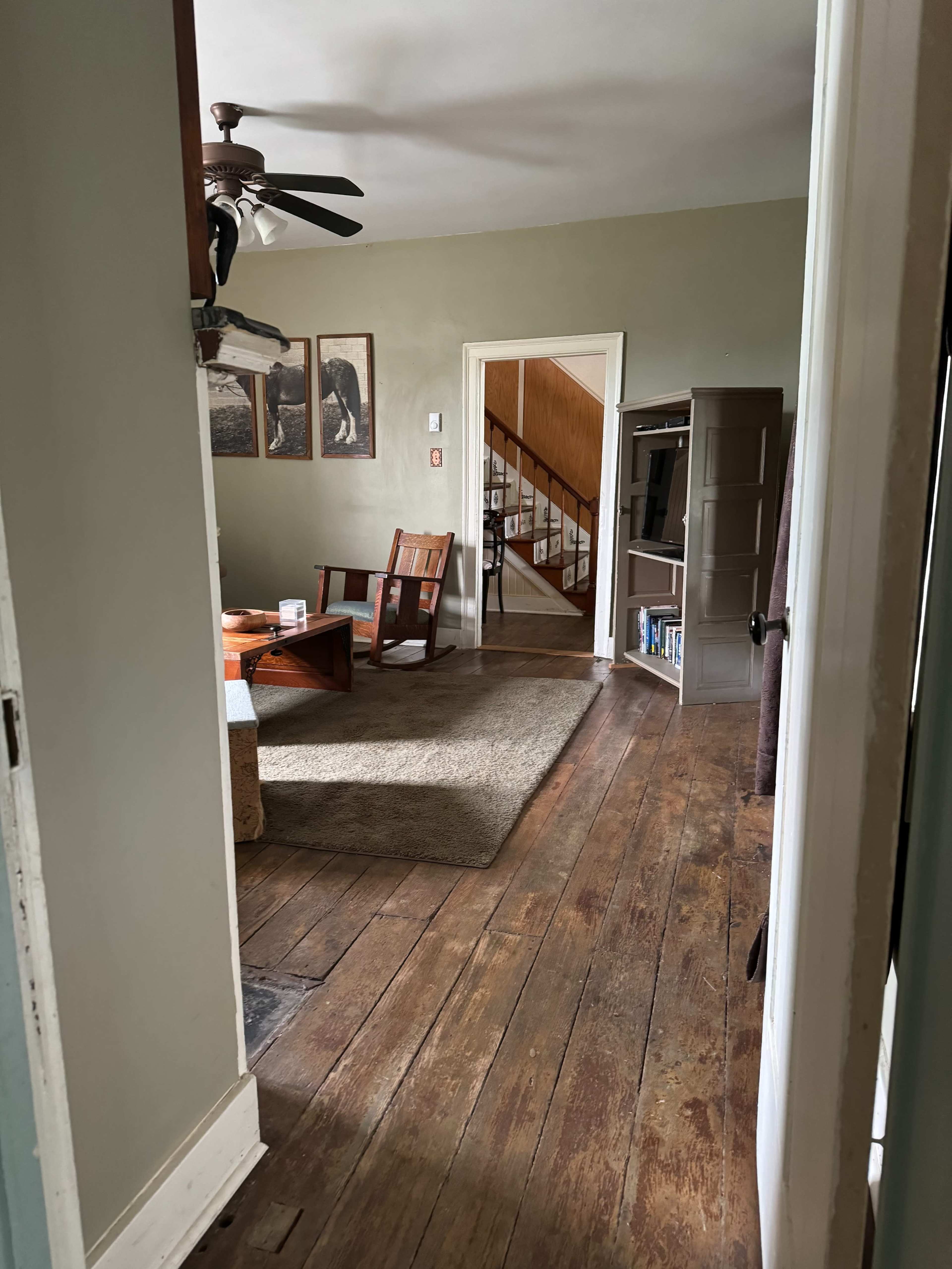 A view from a doorway into a living room, featuring wooden floors, a couple of chairs, and a staircase leading to another level.