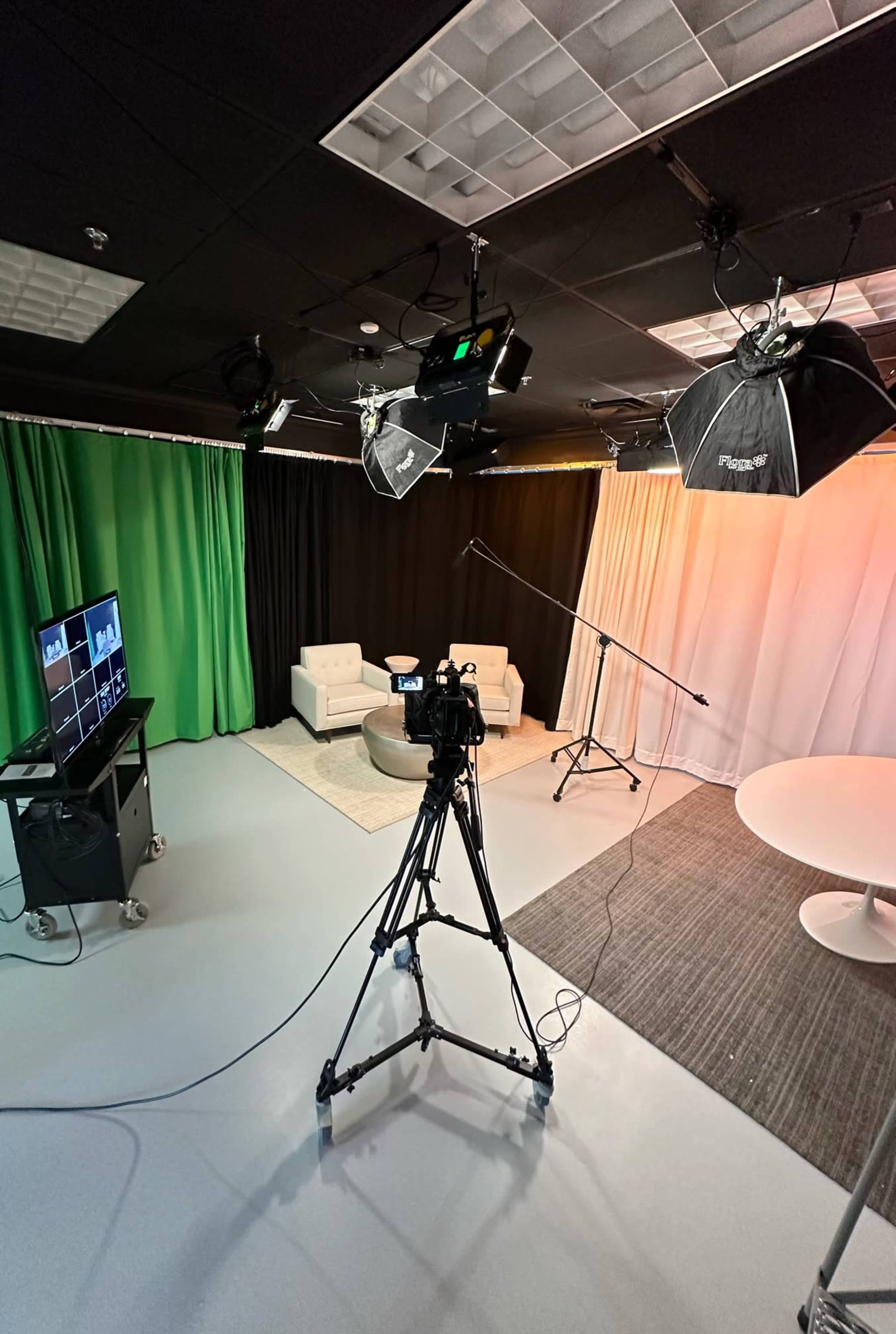A video production studio with a camera on a tripod, lighting equipment, and various backdrops, including green and black curtains.