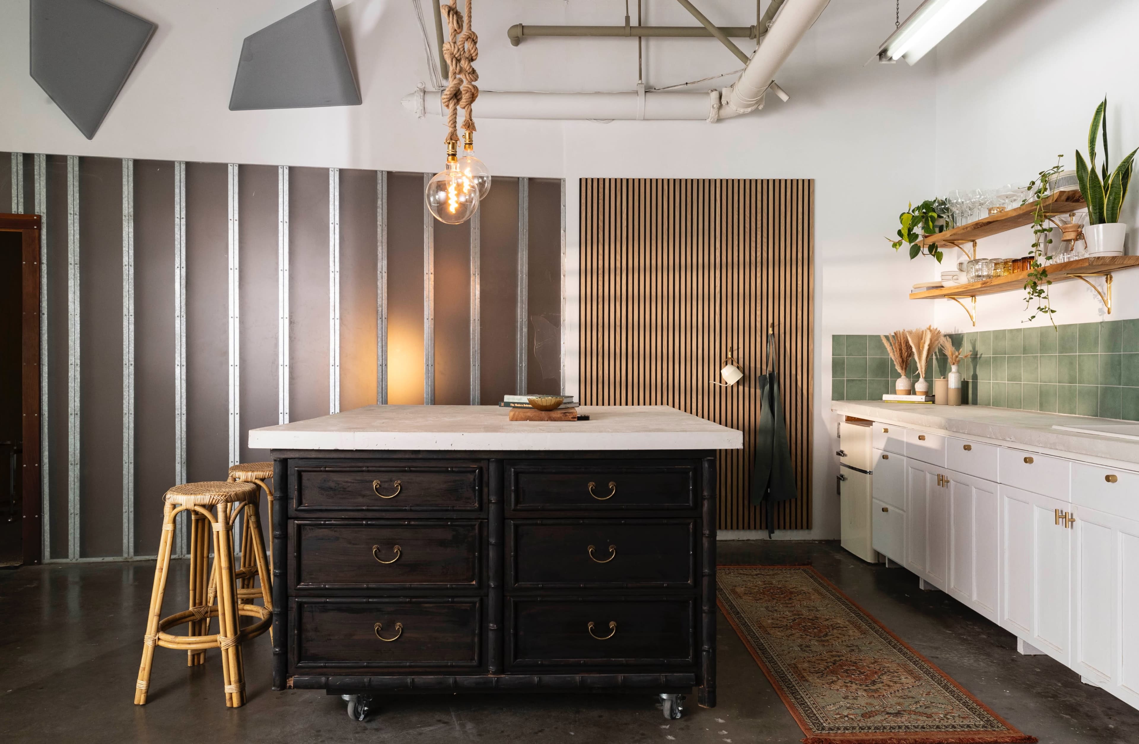 A modern kitchen features a central island with dark cabinets, a pendant light above, and white cabinetry against green tile.