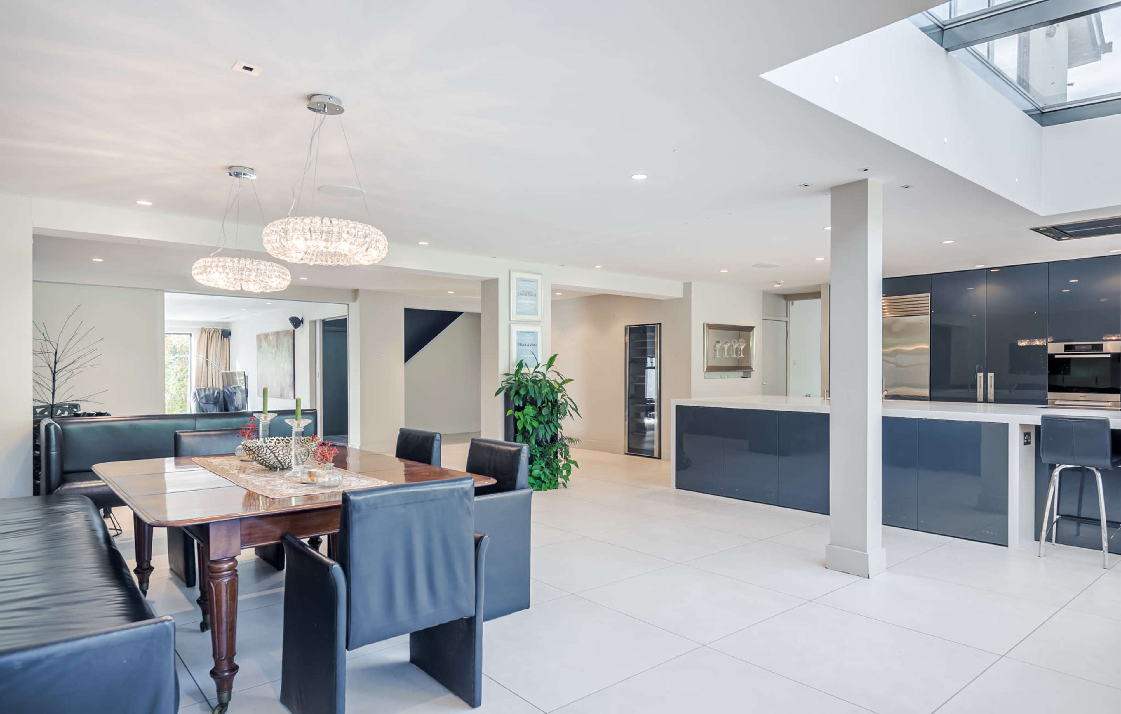 A modern, open-concept living space featuring a dining area with a wooden table and black chairs, a sleek kitchen, and large windows allowing natural light.