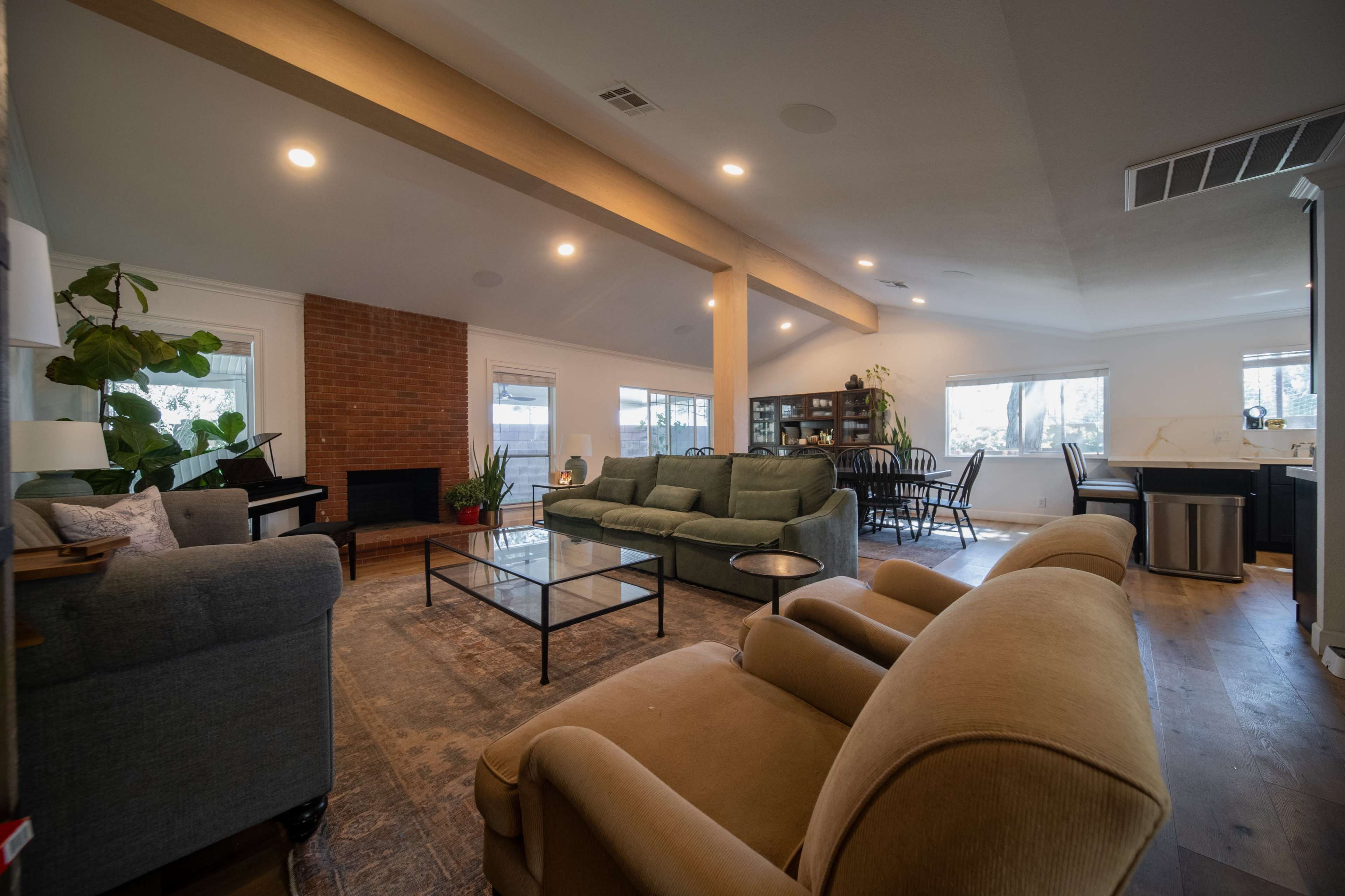 The image shows a spacious living area featuring a sectional sofa, an armchair, a coffee table, a dining table, and a brick fireplace.