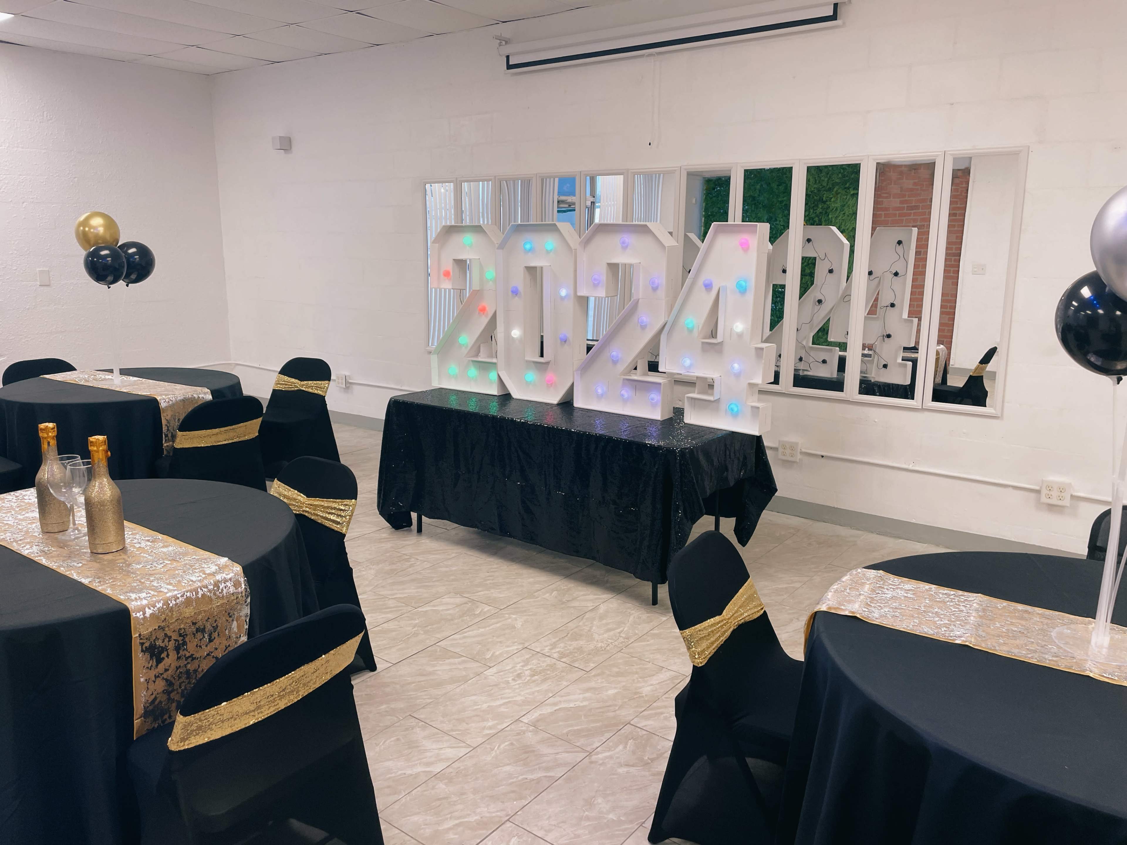 A decorated event space features black and gold tables, a large illuminated "2024" display, and a mirrored backdrop.