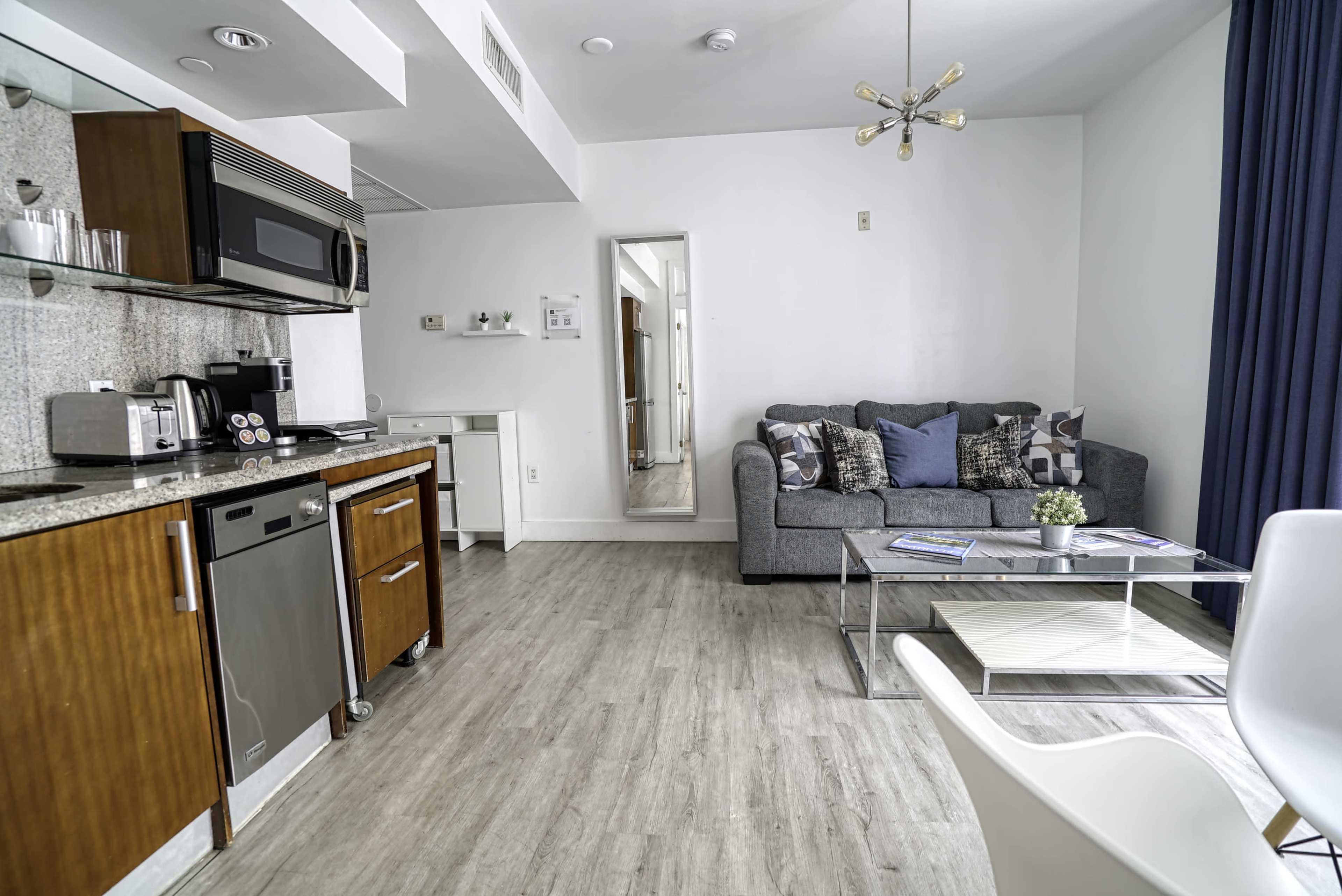 The image shows a modern living area with a kitchen, a sofa, a coffee table, and a mirror mounted on the wall.