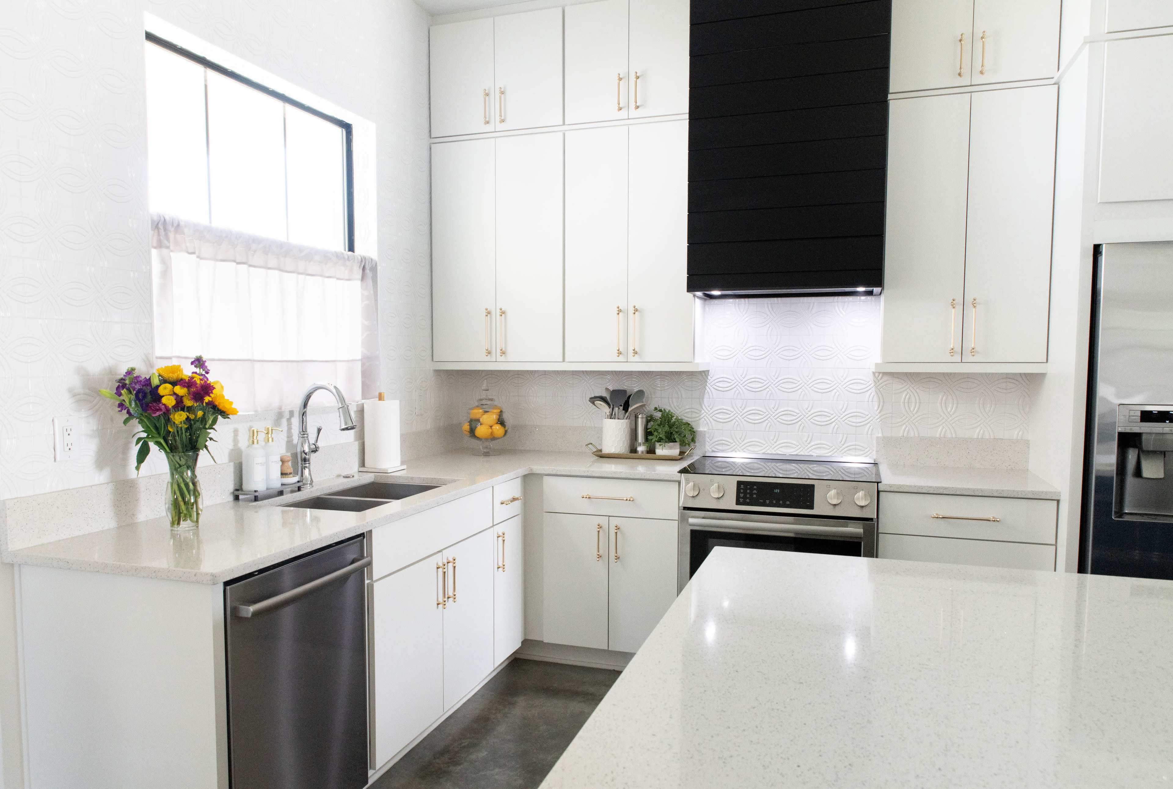 A modern kitchen features white cabinetry, stainless steel appliances, and a large island with a light-colored countertop.