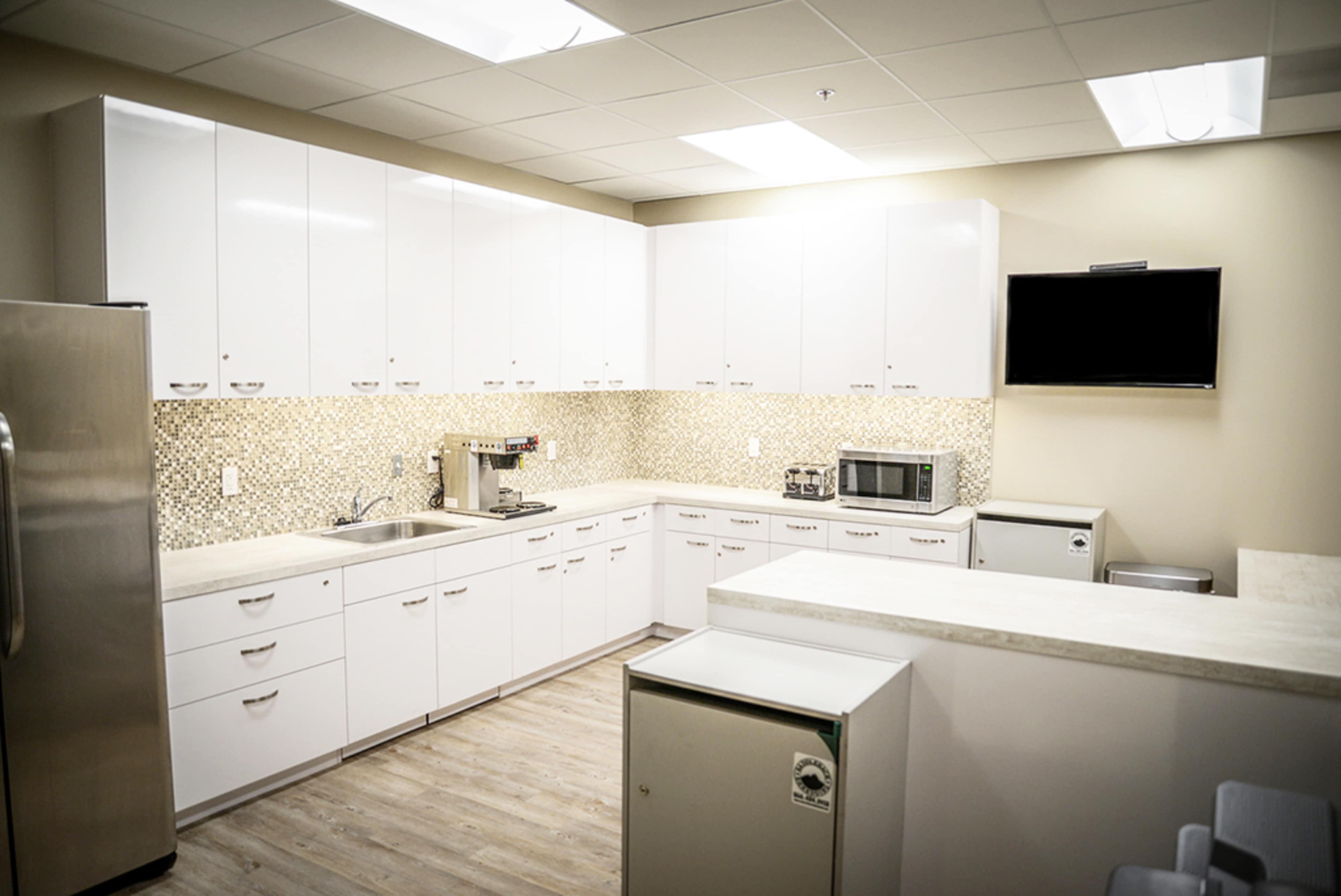 A modern kitchen with white cabinets, a stainless steel refrigerator, and a countertop equipped with various appliances.