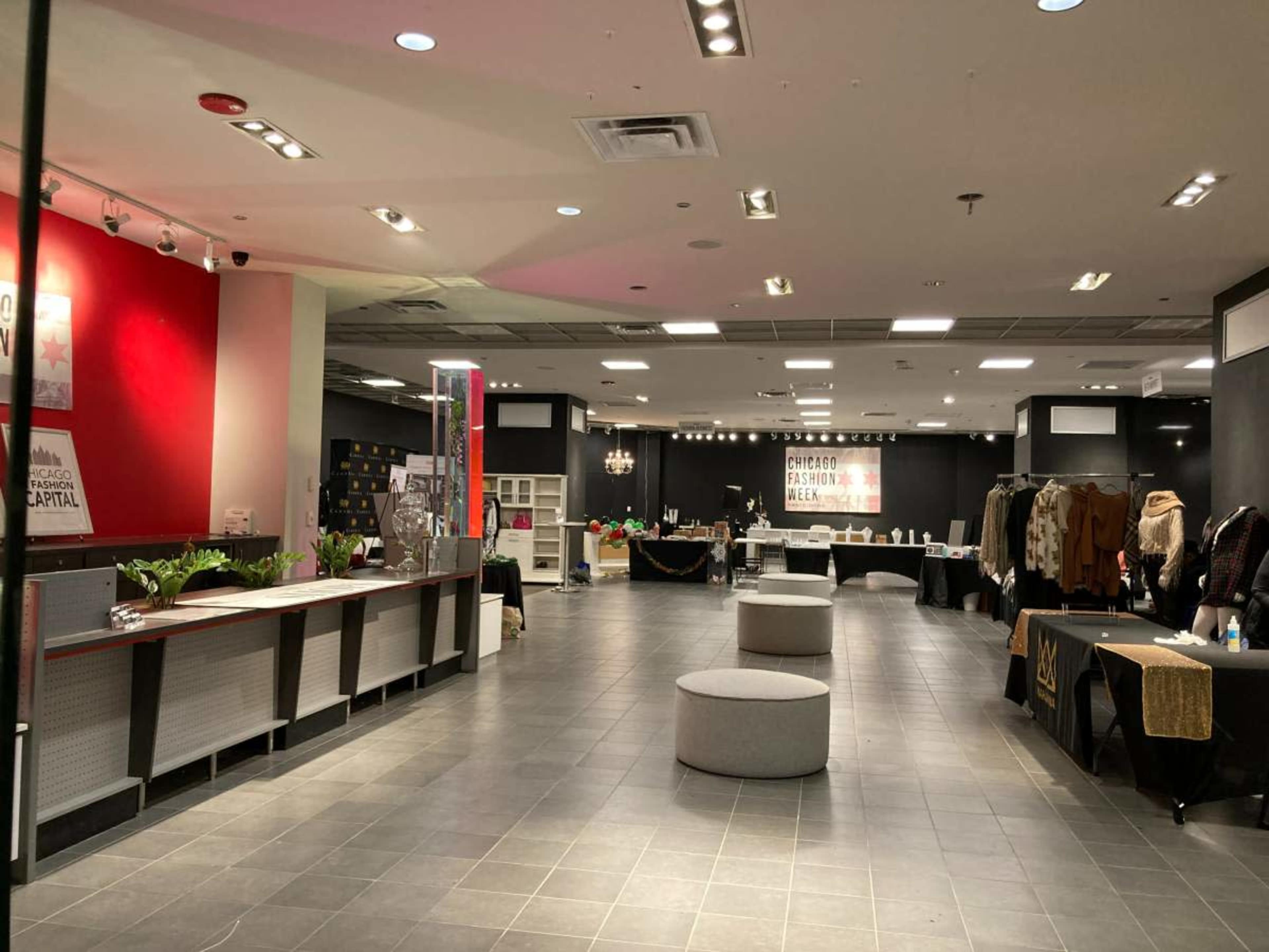 The image shows a spacious, modern interior of a retail space with various display tables, a circular seating area, and promotional signage on the walls.