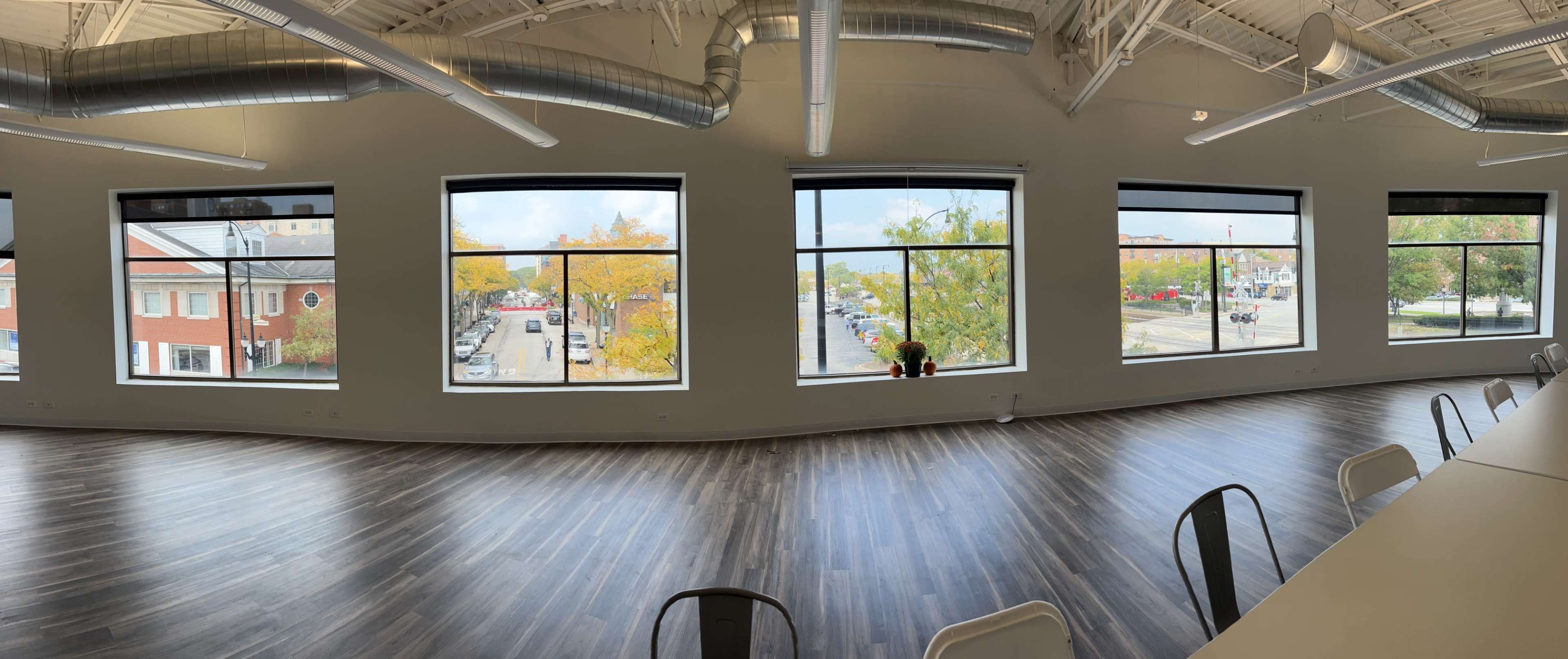 A spacious interior with large windows overlooking a street lined with trees and buildings.