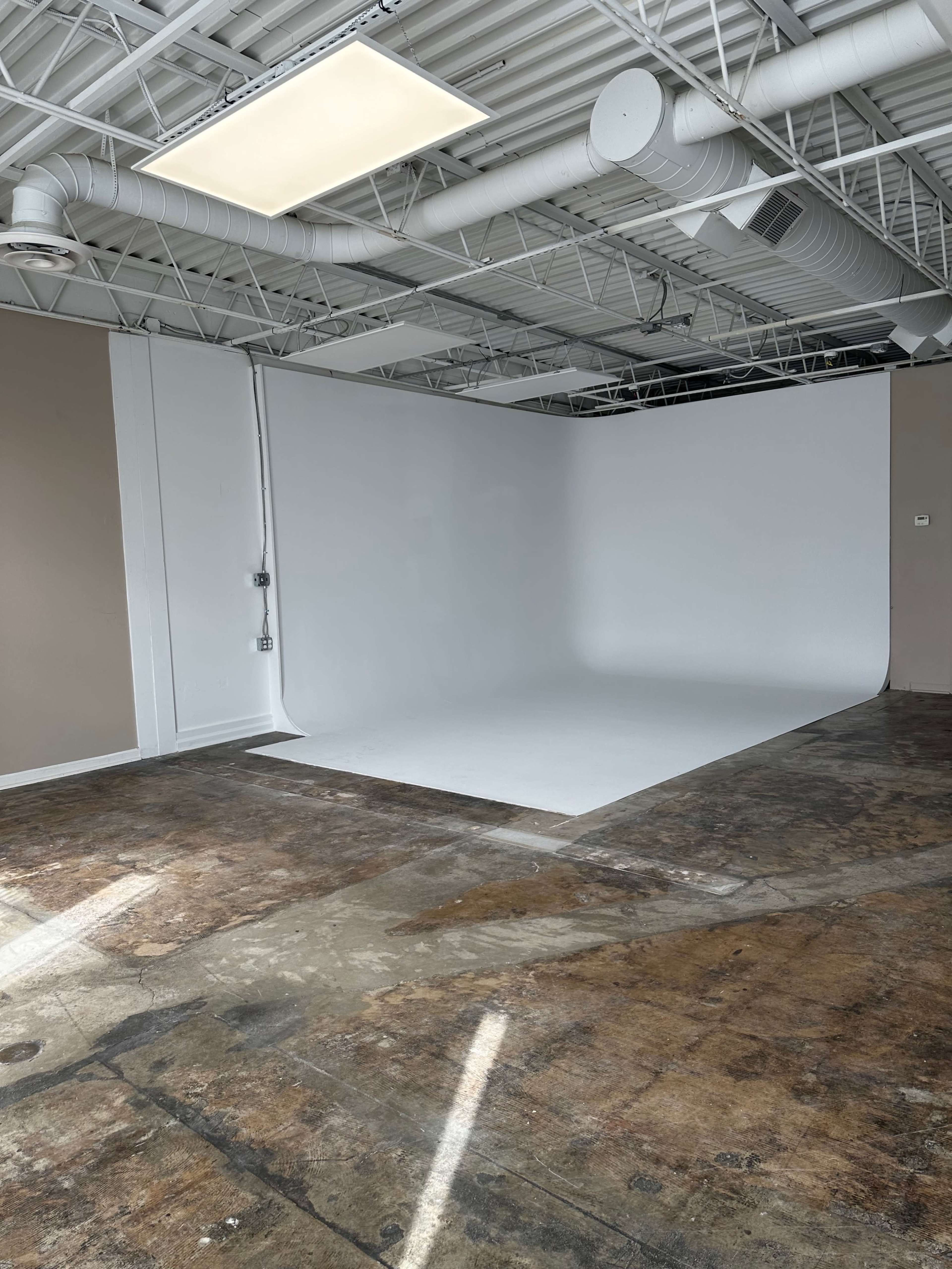 An empty studio space with a white backdrop and a concrete floor.