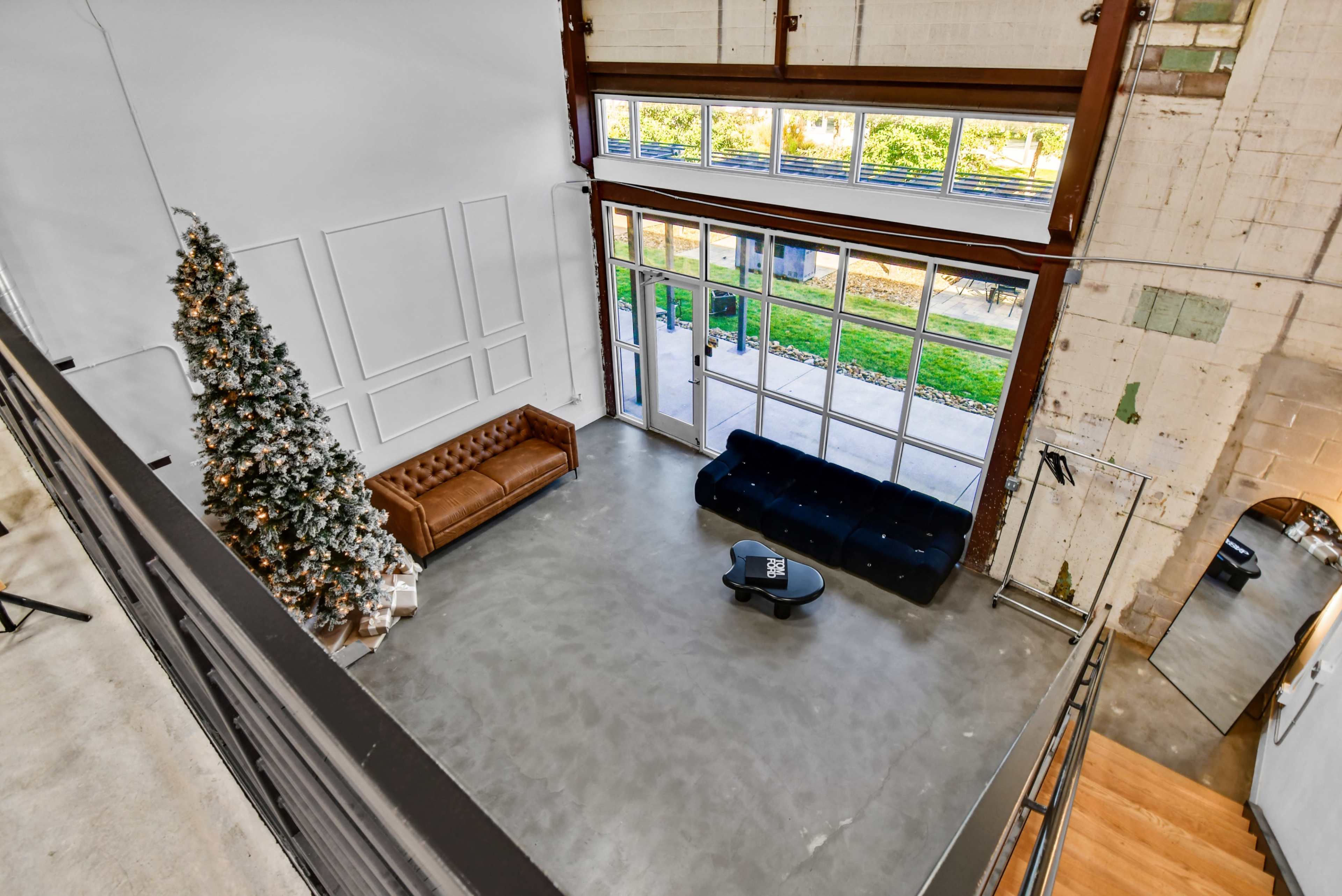 The image shows a spacious interior with a large window, a leather couch, a black sofa, a coffee table, and a Christmas tree.