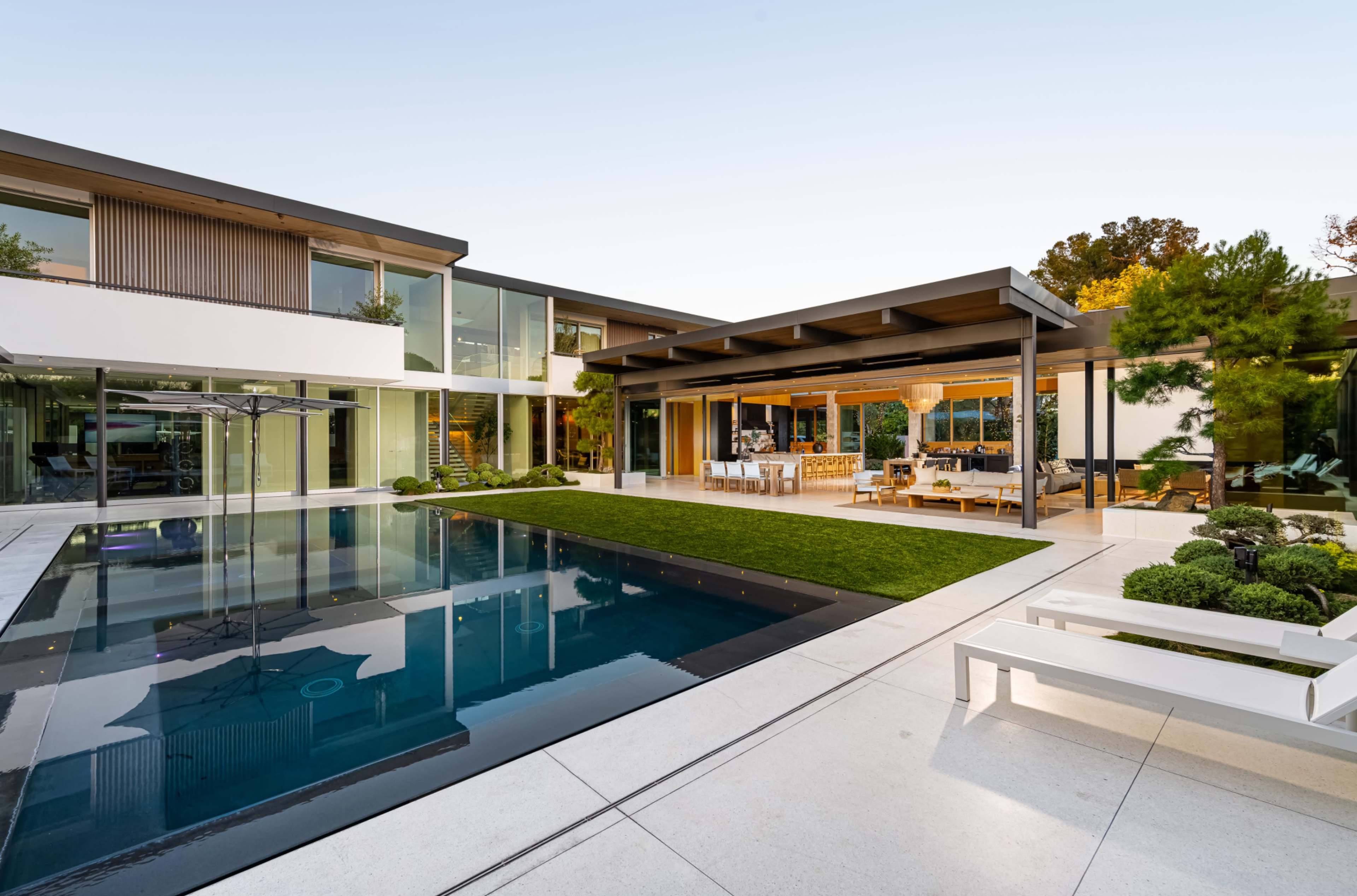 A modern home features a sleek pool surrounded by landscaped greenery and a covered outdoor seating area.