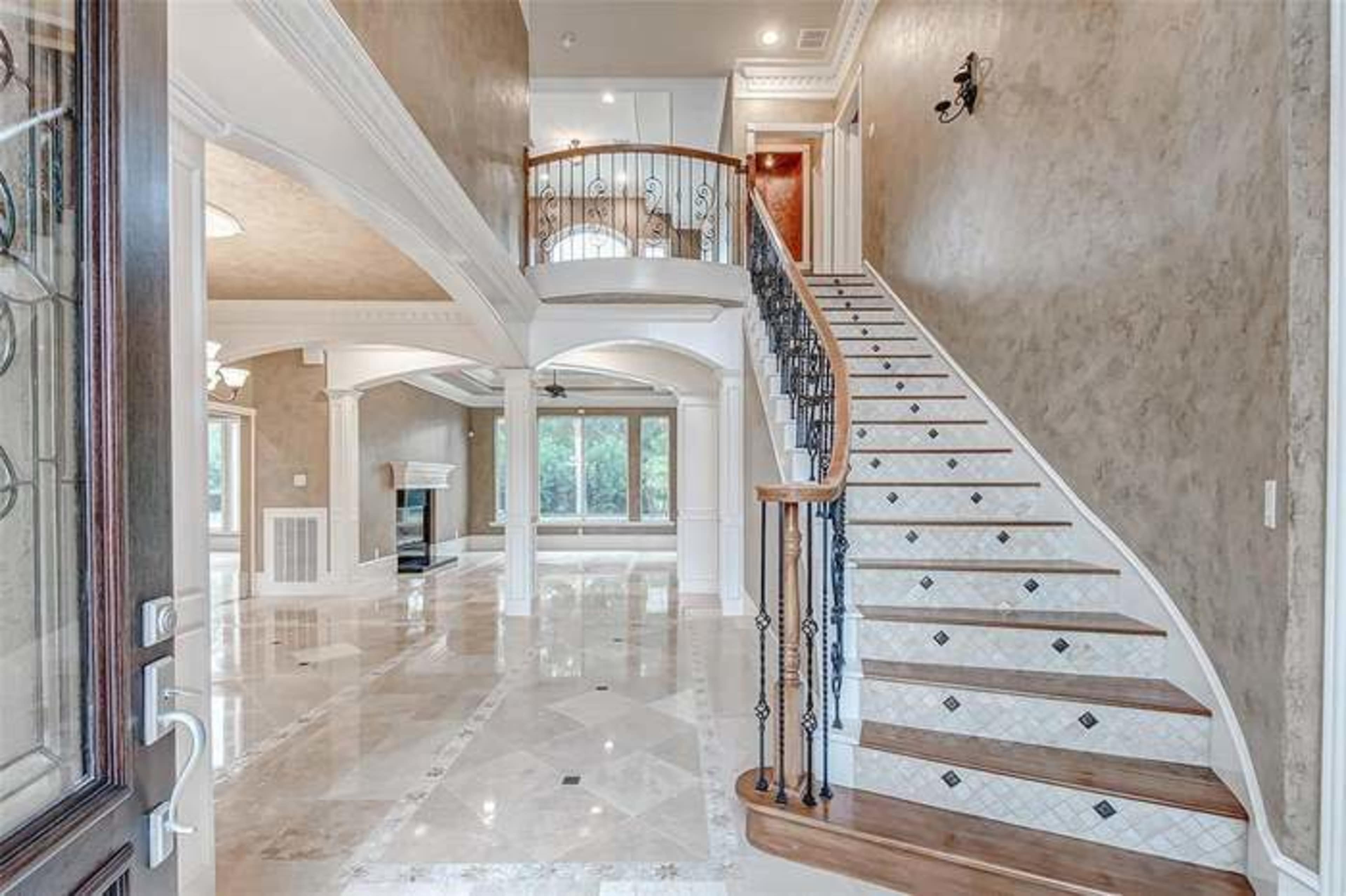A spacious foyer with a curved staircase and marble floors leading to a living area with large windows.