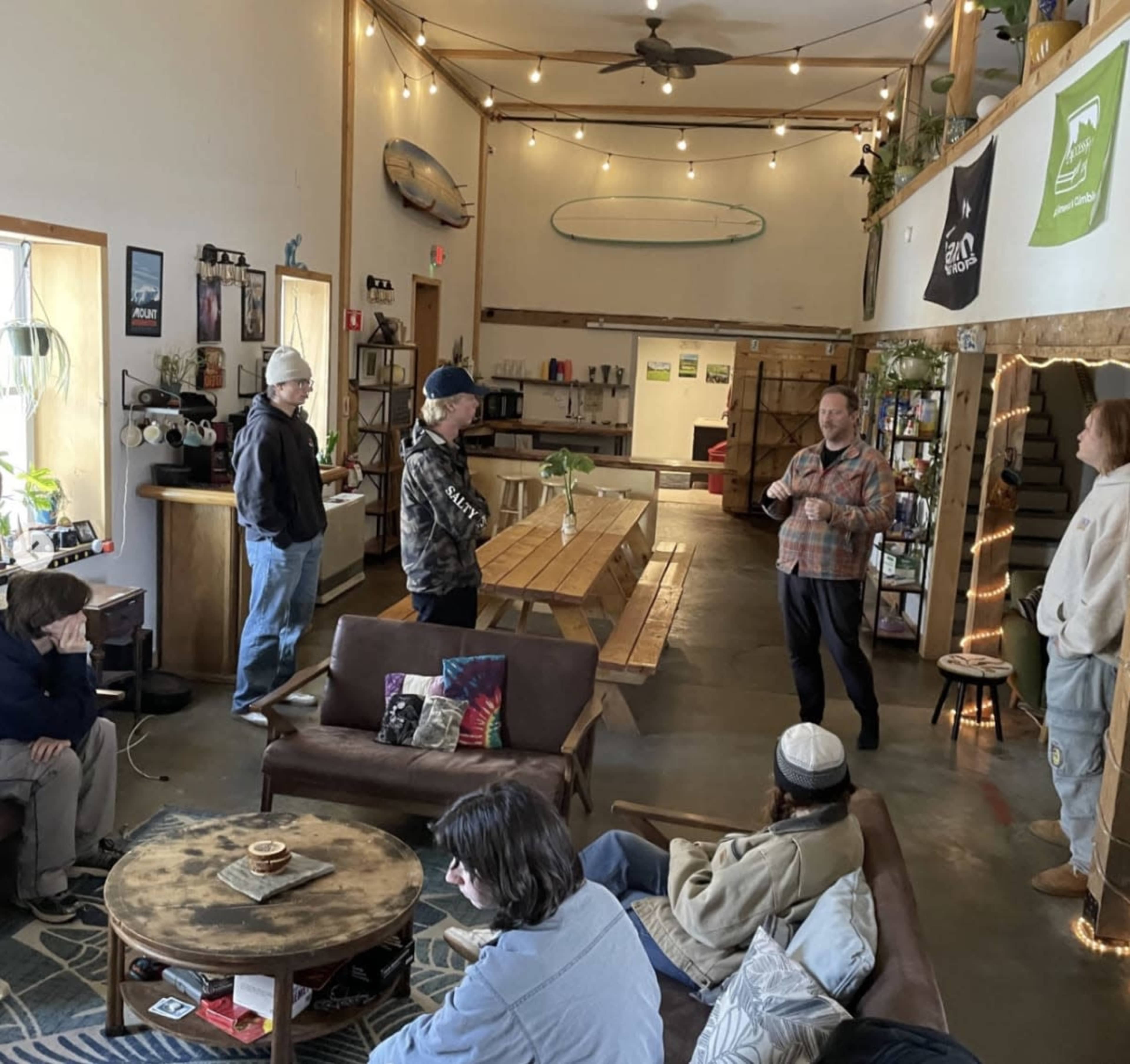 A group of people are engaged in conversation in a spacious, well-lit indoor space with wooden tables and cozy seating.
