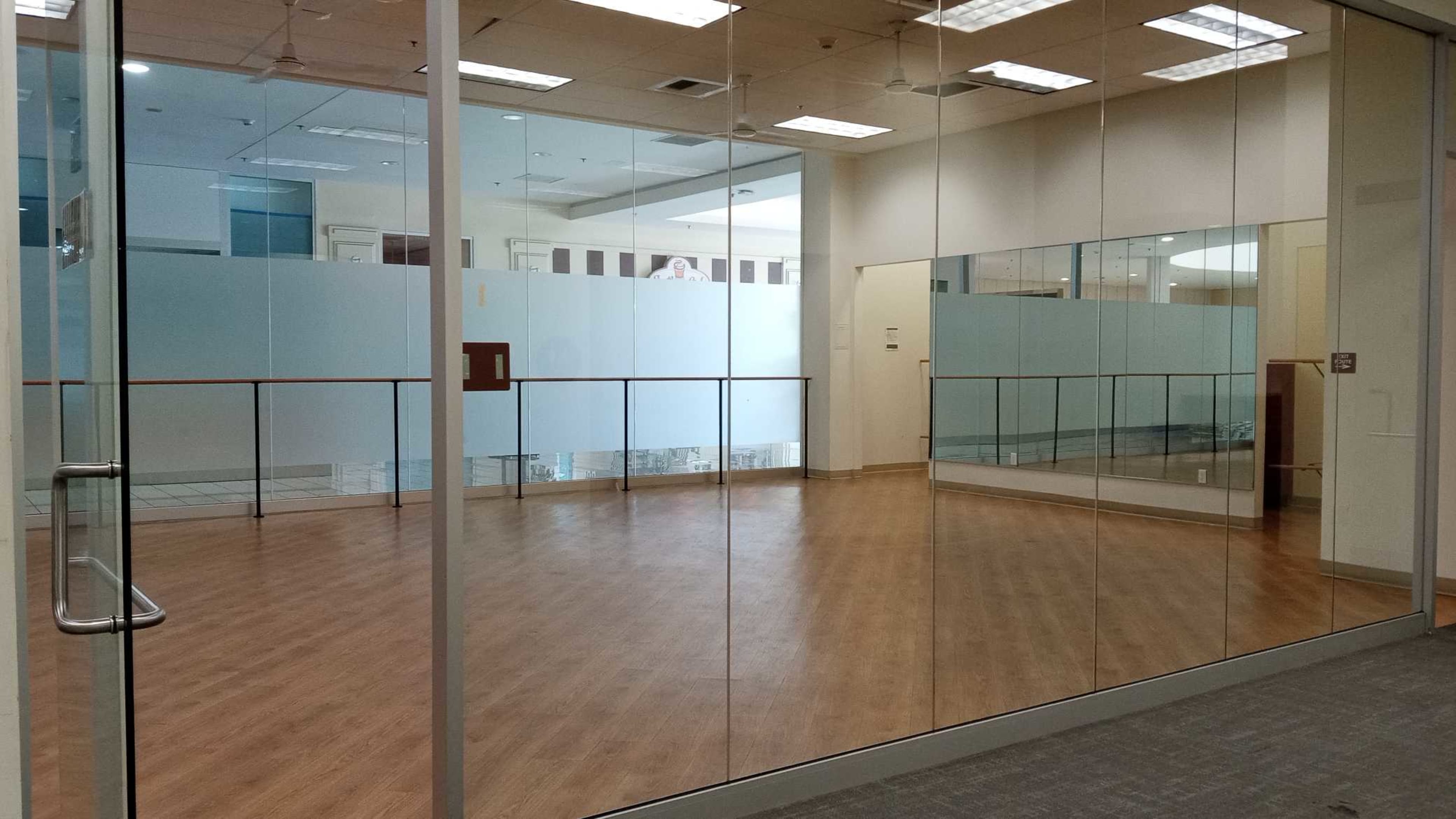 The image shows a large, empty studio space with glass walls and wooden flooring.