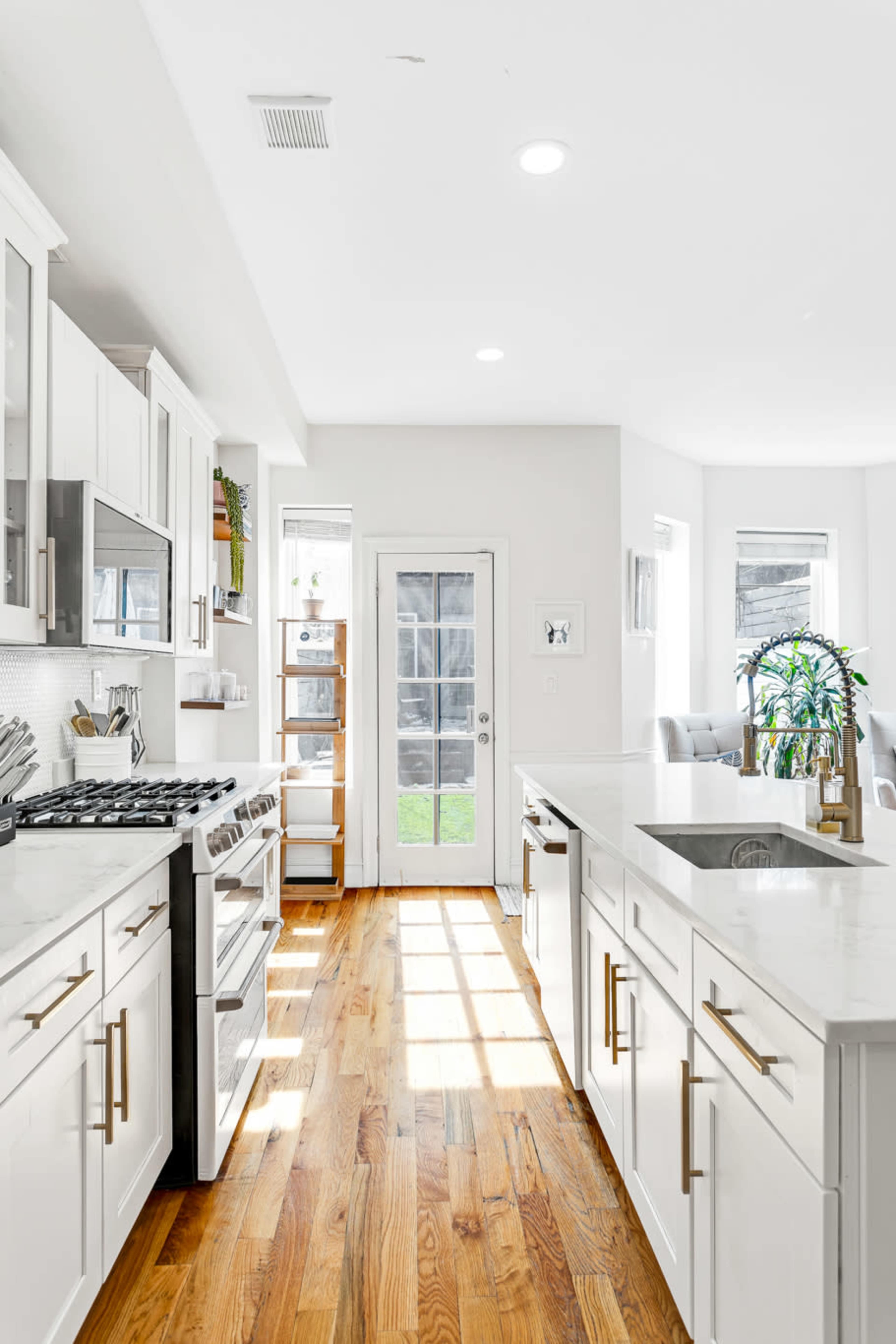 The kitchen features white cabinetry, a stainless steel gas stove, a marble countertop, and a door leading to an outdoor area, illuminated by natural light.