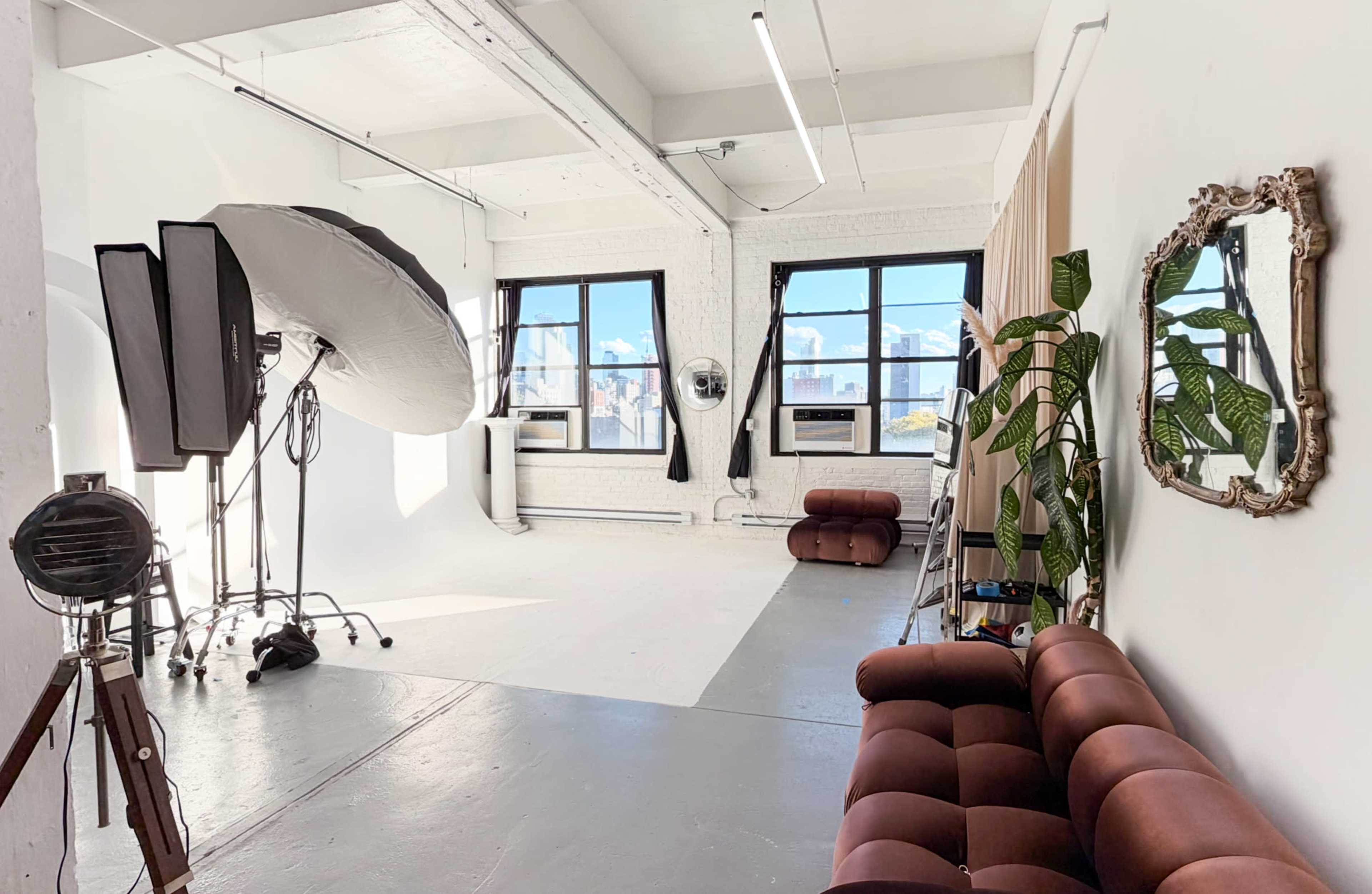 The image shows a well-lit photography studio with large windows, modern furniture, and a backdrop setup.