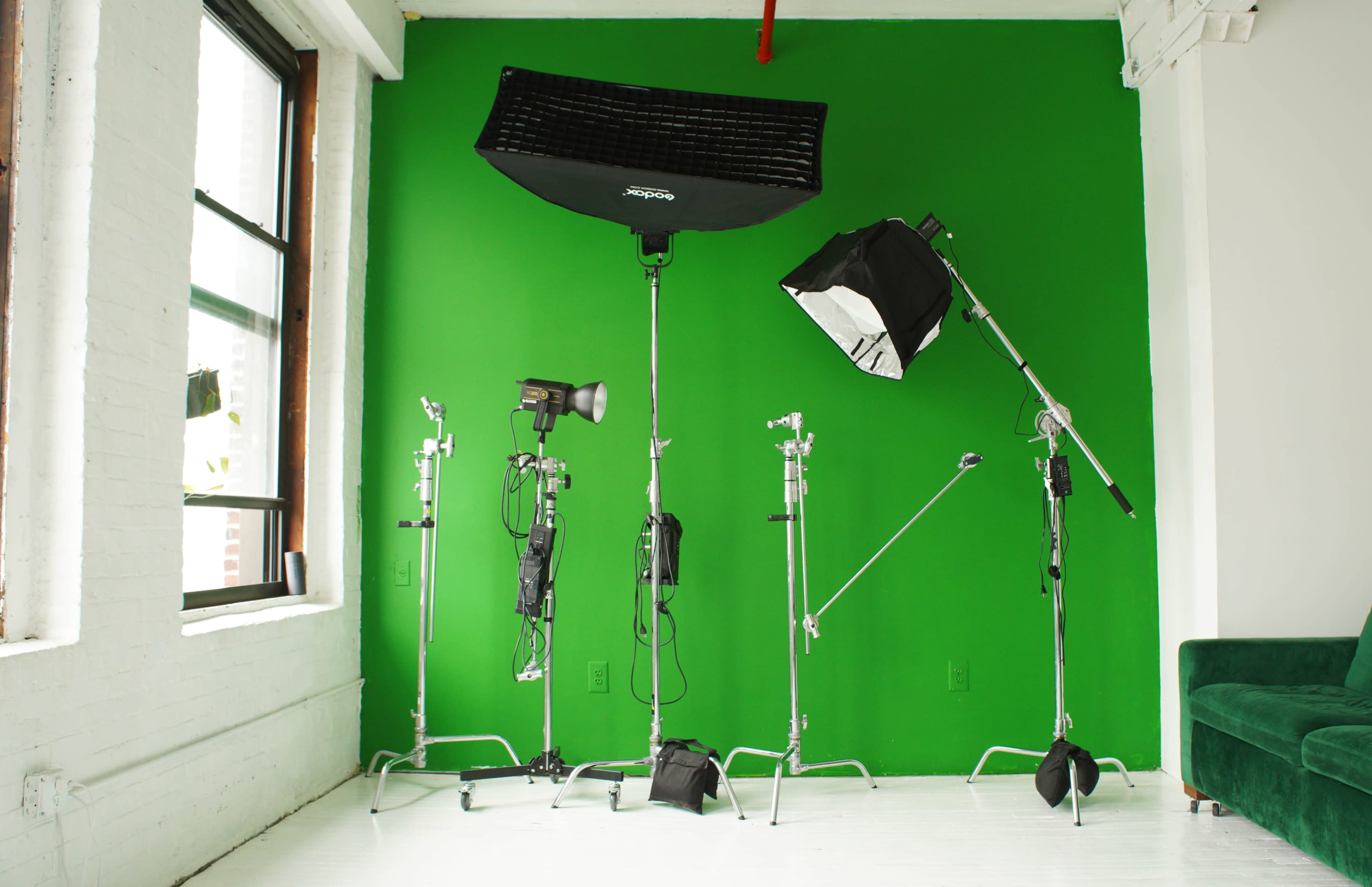 A studio setup with various lighting equipment positioned against a green backdrop.