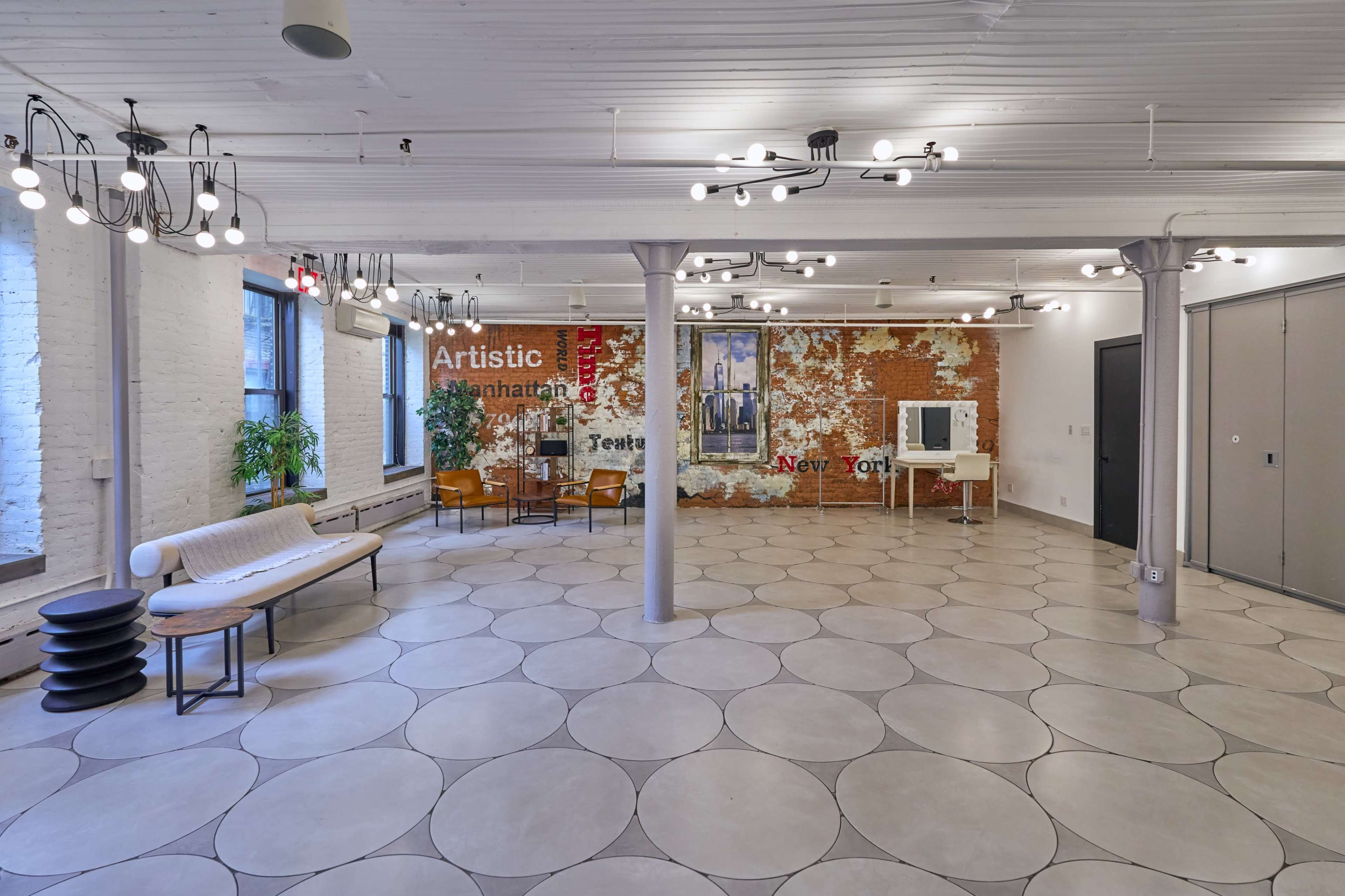 A spacious, modern interior features a polished concrete floor, exposed brick wall, and various seating arrangements under industrial-style lighting.