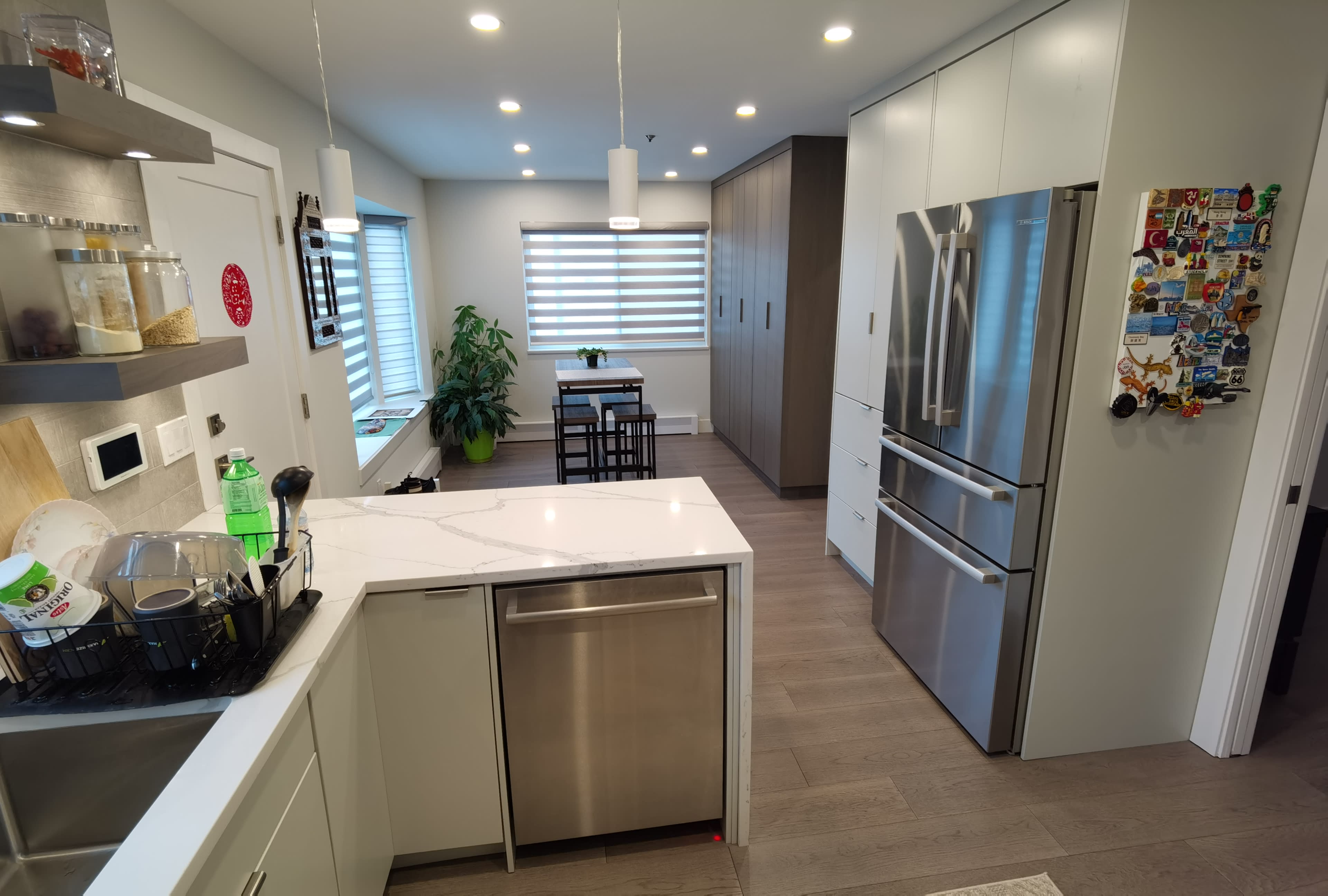 A modern kitchen features stainless steel appliances, white cabinetry, and a small dining area with a table and chairs near a window.