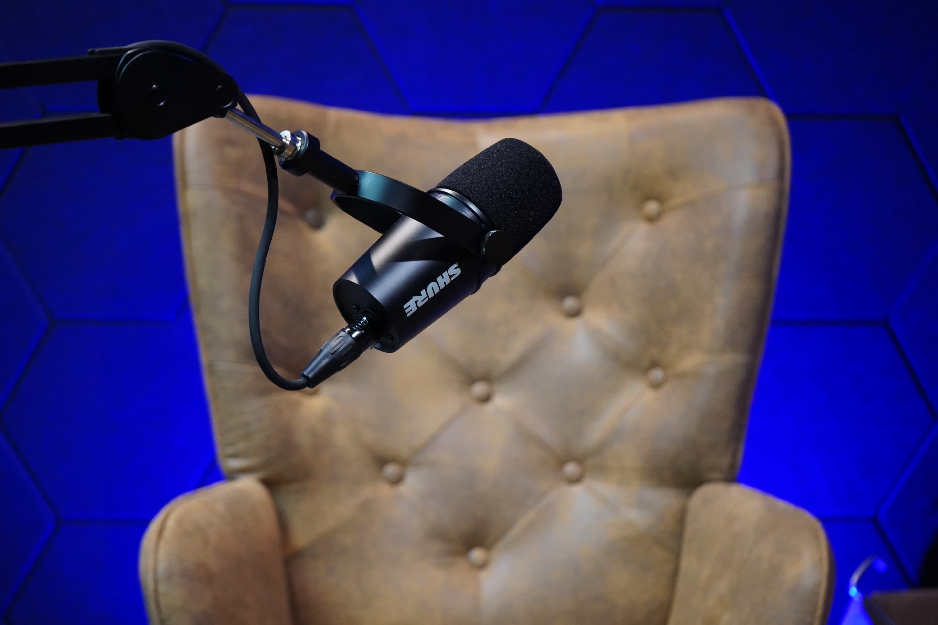 A microphone is mounted on a black arm above a brown leather chair in front of a blue, hexagonal-patterned backdrop.