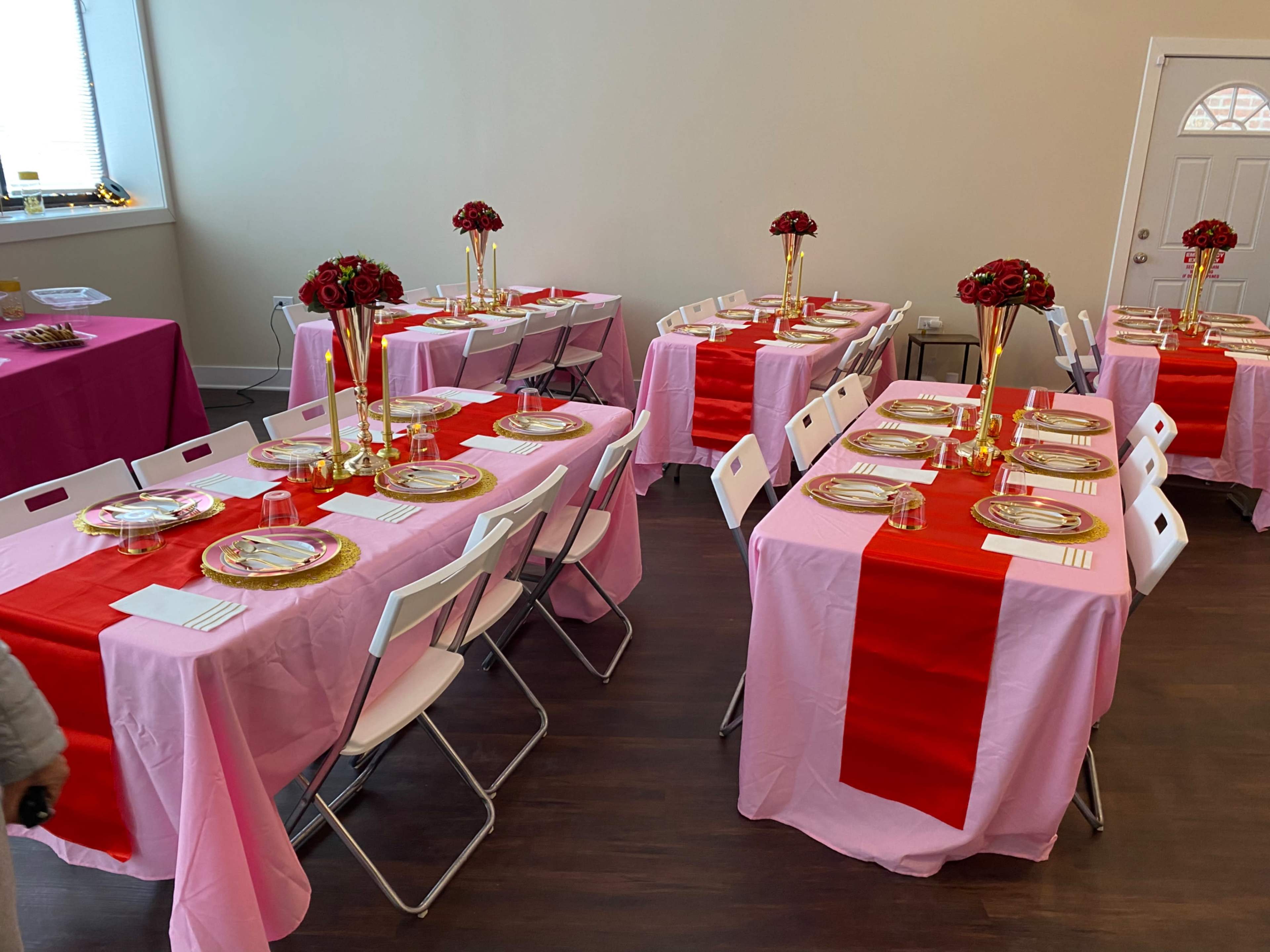 A decorated room with several tables set with pink and red tablecloths, gold plates, and flower centerpieces.