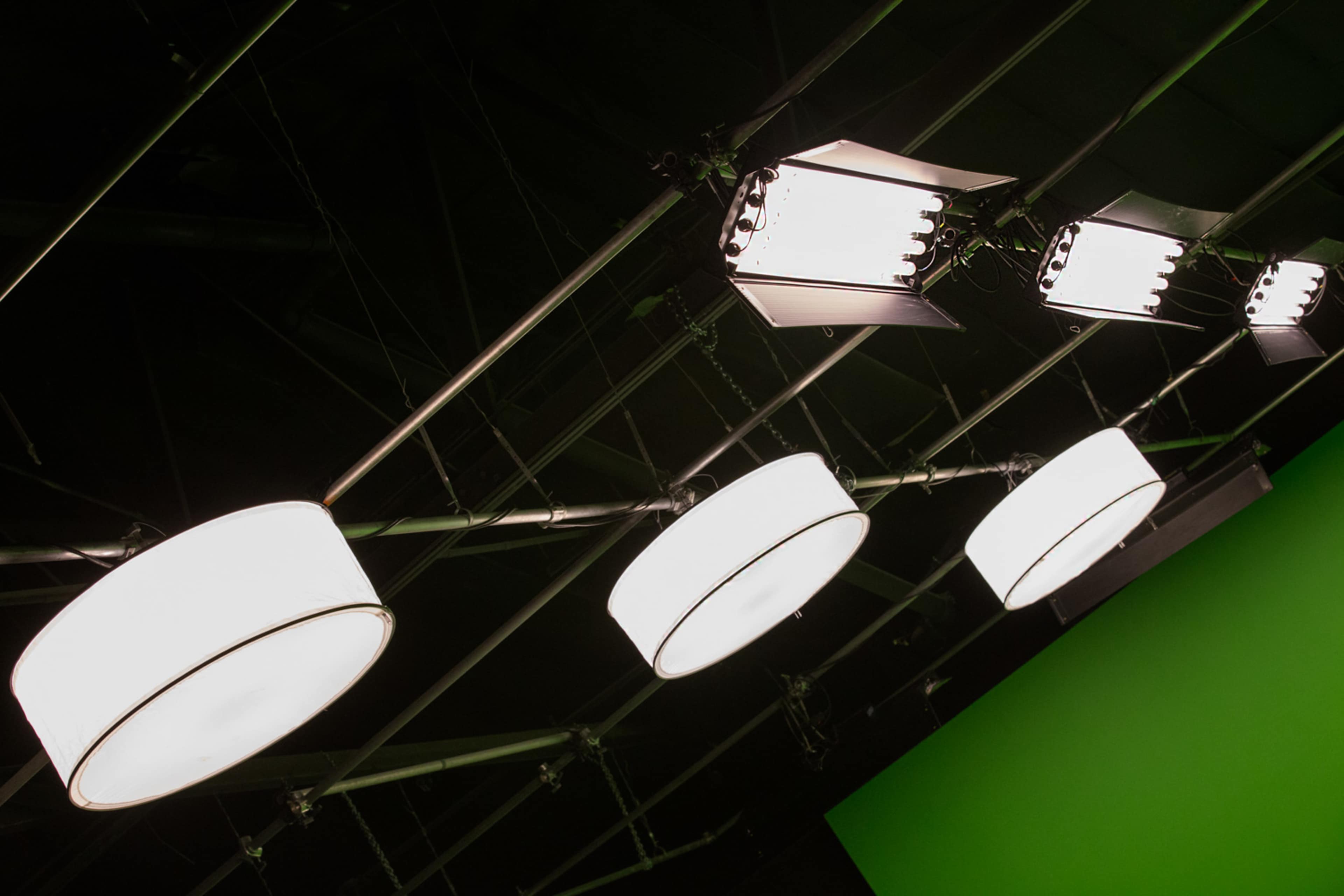 Several overhead studio lights mounted on a black ceiling, with a green backdrop visible in the background.