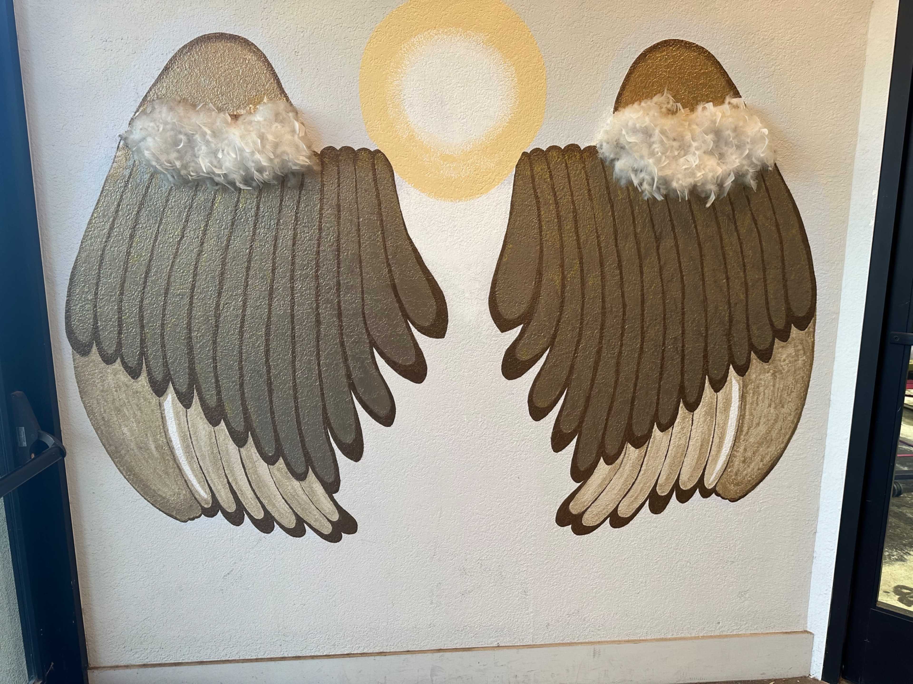 The image features a mural of two large, stylized wings with a circular light source above them, all painted on a white wall.