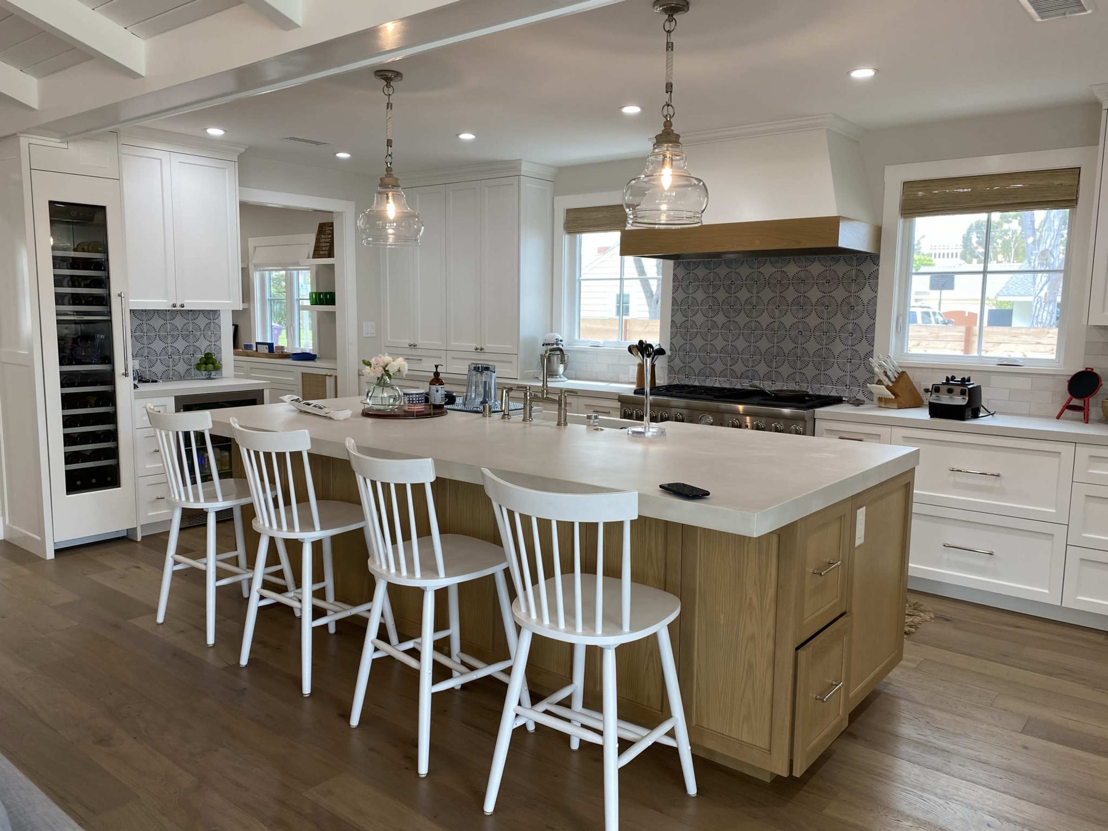 A modern kitchen with a central island, four white wooden bar stools, and various appliances and fixtures.