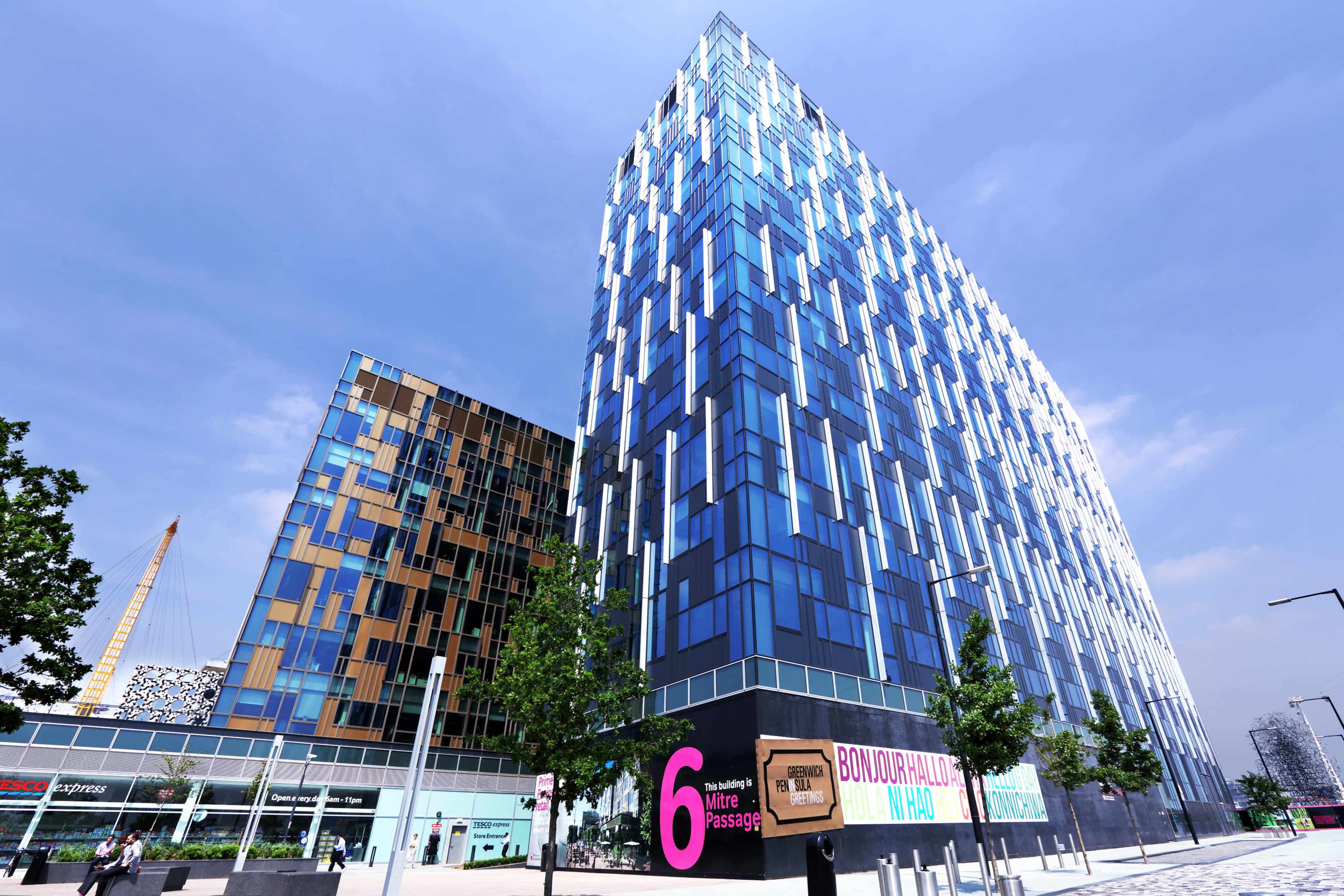 Two modern buildings with colorful facades, set in an urban environment with trees and clear skies.