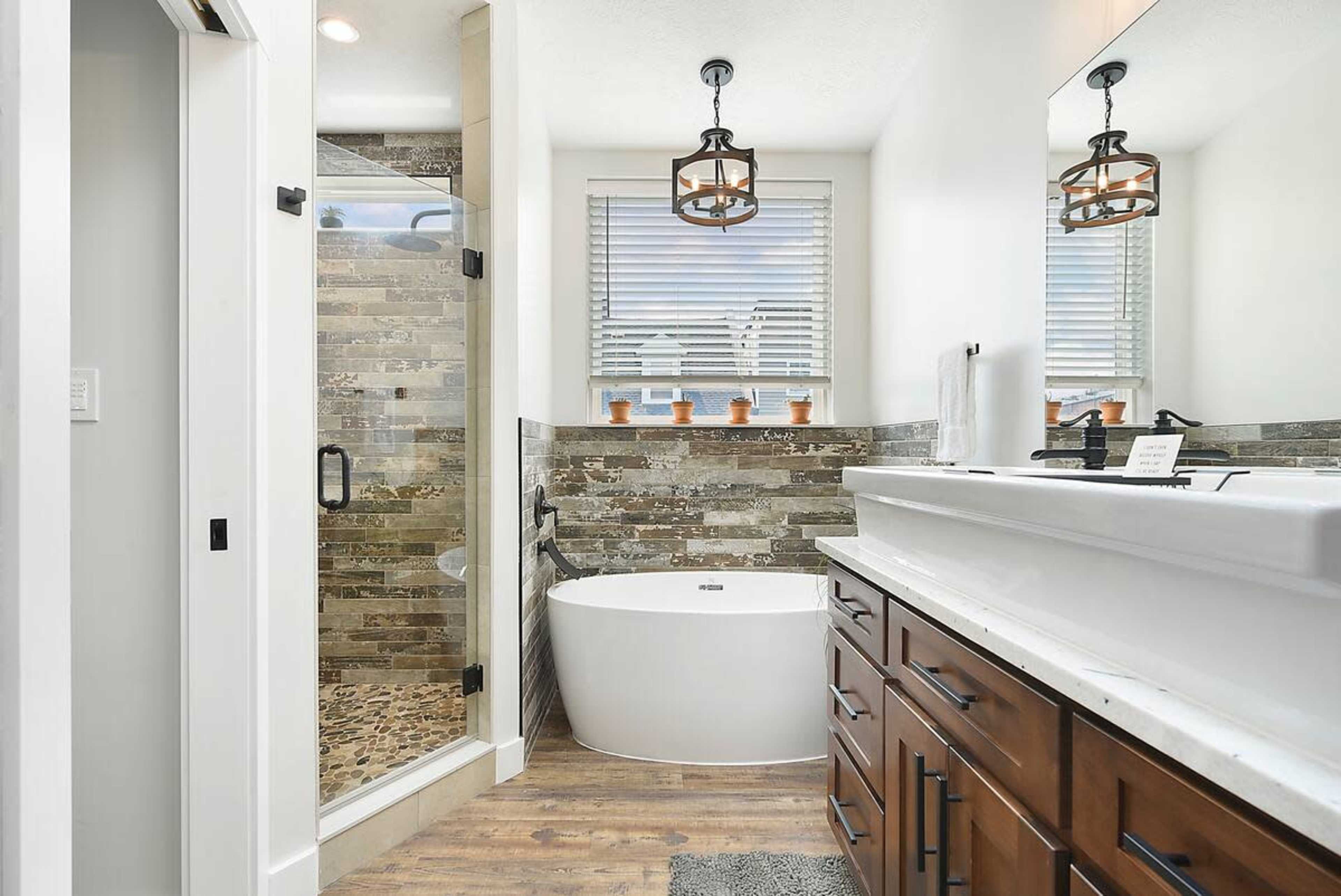 The bathroom features a freestanding tub, a glass-enclosed shower, and a double vanity with wooden cabinets, complemented by tiled walls and natural light from a window.