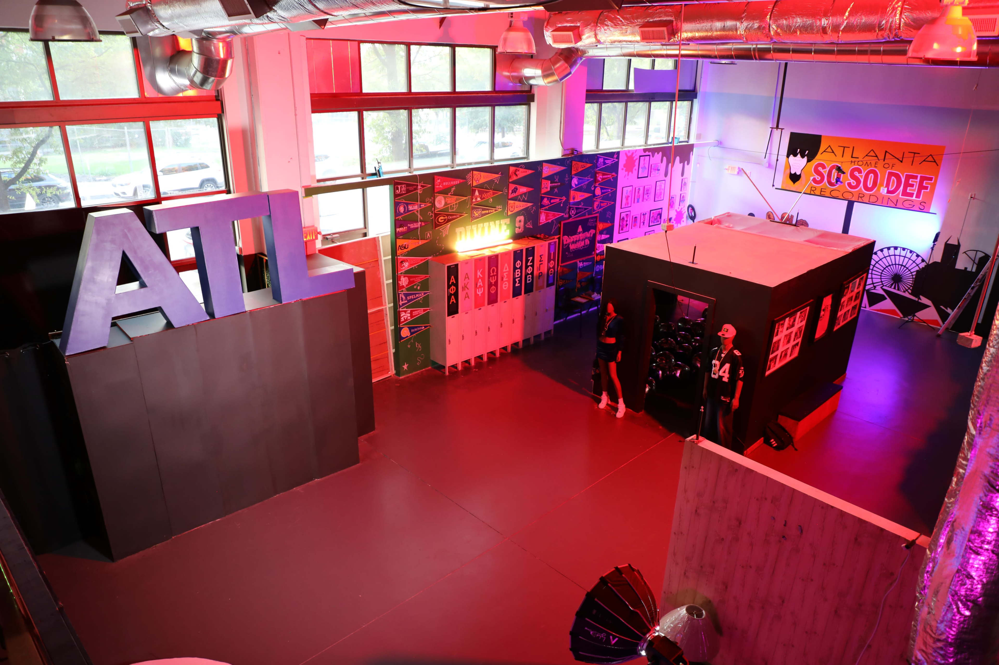 The image shows a large indoor space featuring an oversized "ATL" sign, colorful banners, lockers, and a black structure resembling a room.