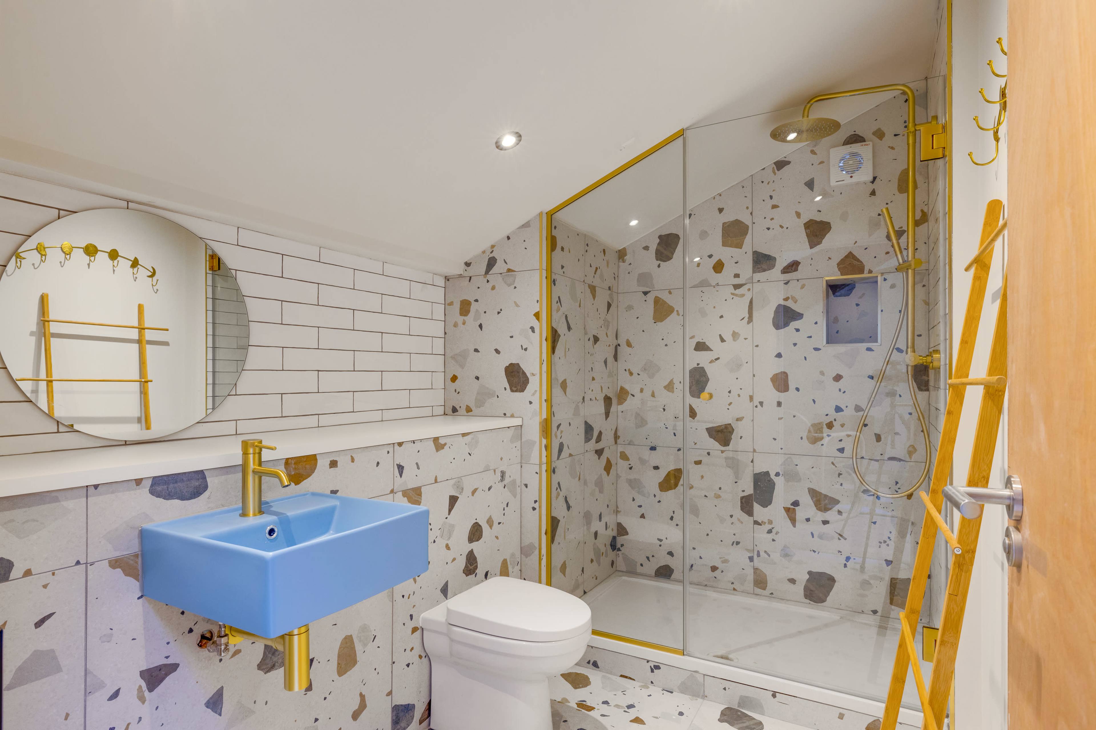 A modern bathroom featuring a blue sink, a glass shower with patterned walls, and yellow accents throughout.