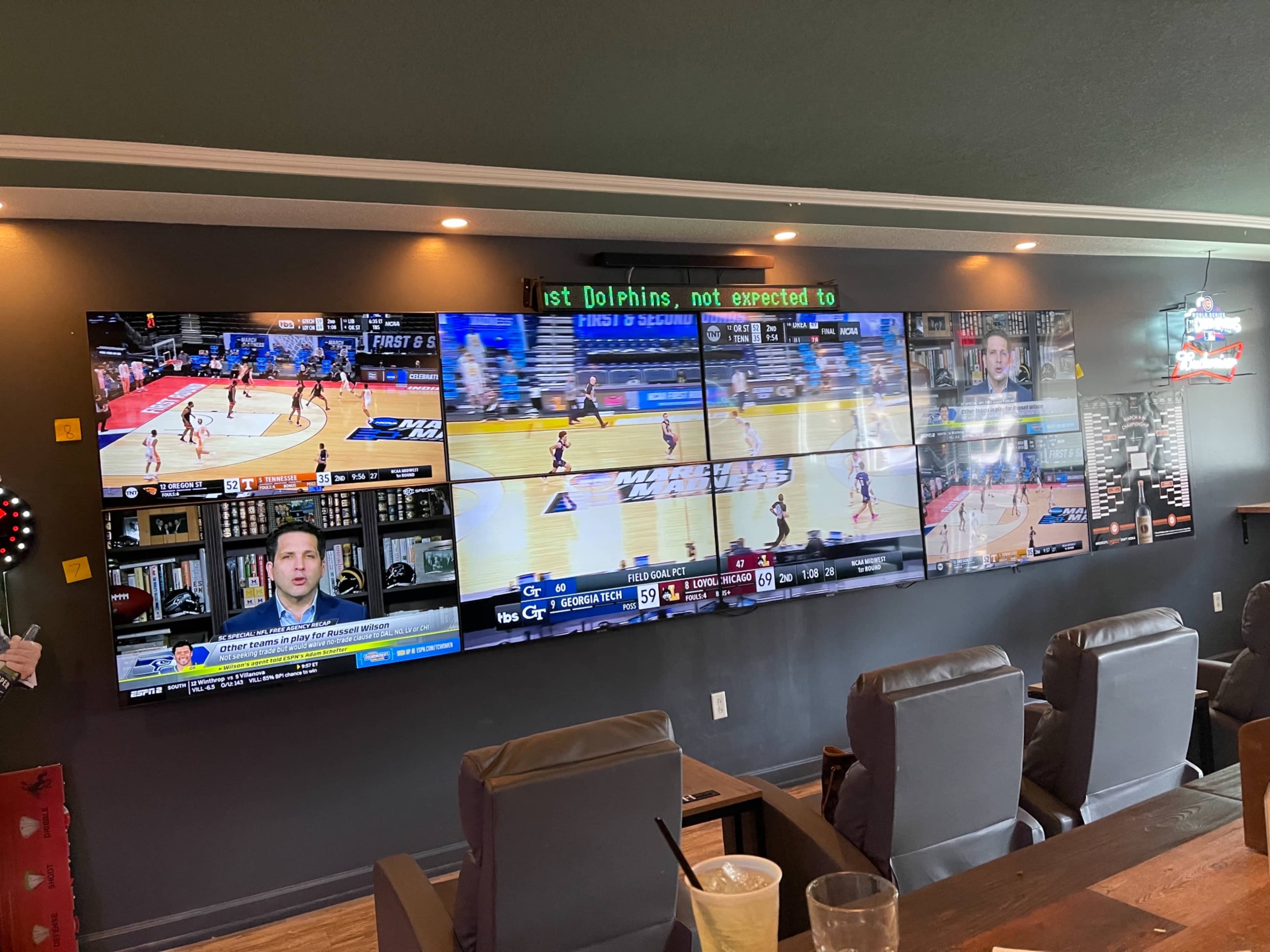 A wall-mounted array of multiple large television screens displaying various sports events and news updates in a lounge setting.