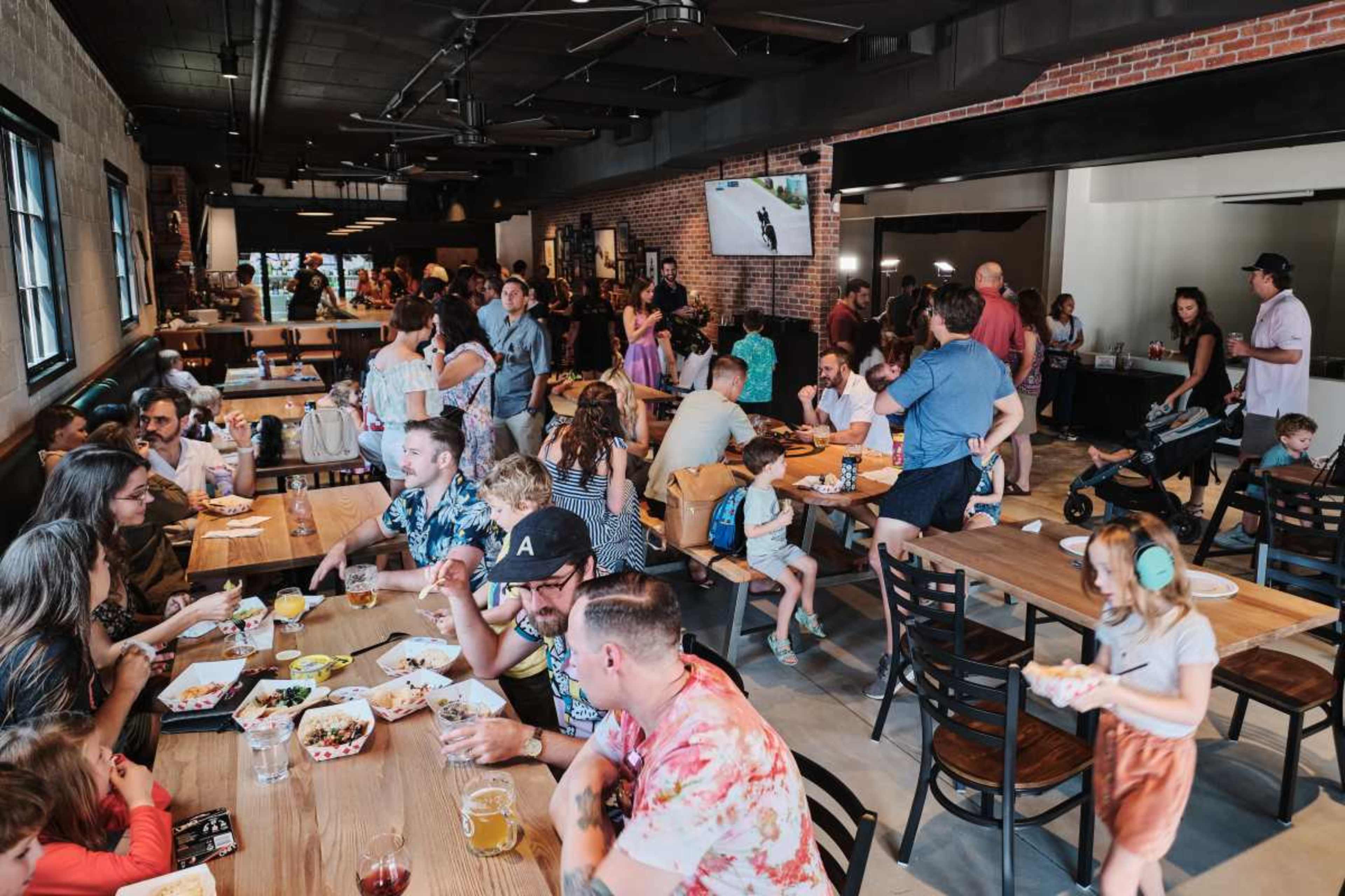 A busy restaurant interior filled with families and groups enjoying their meals at wooden tables.