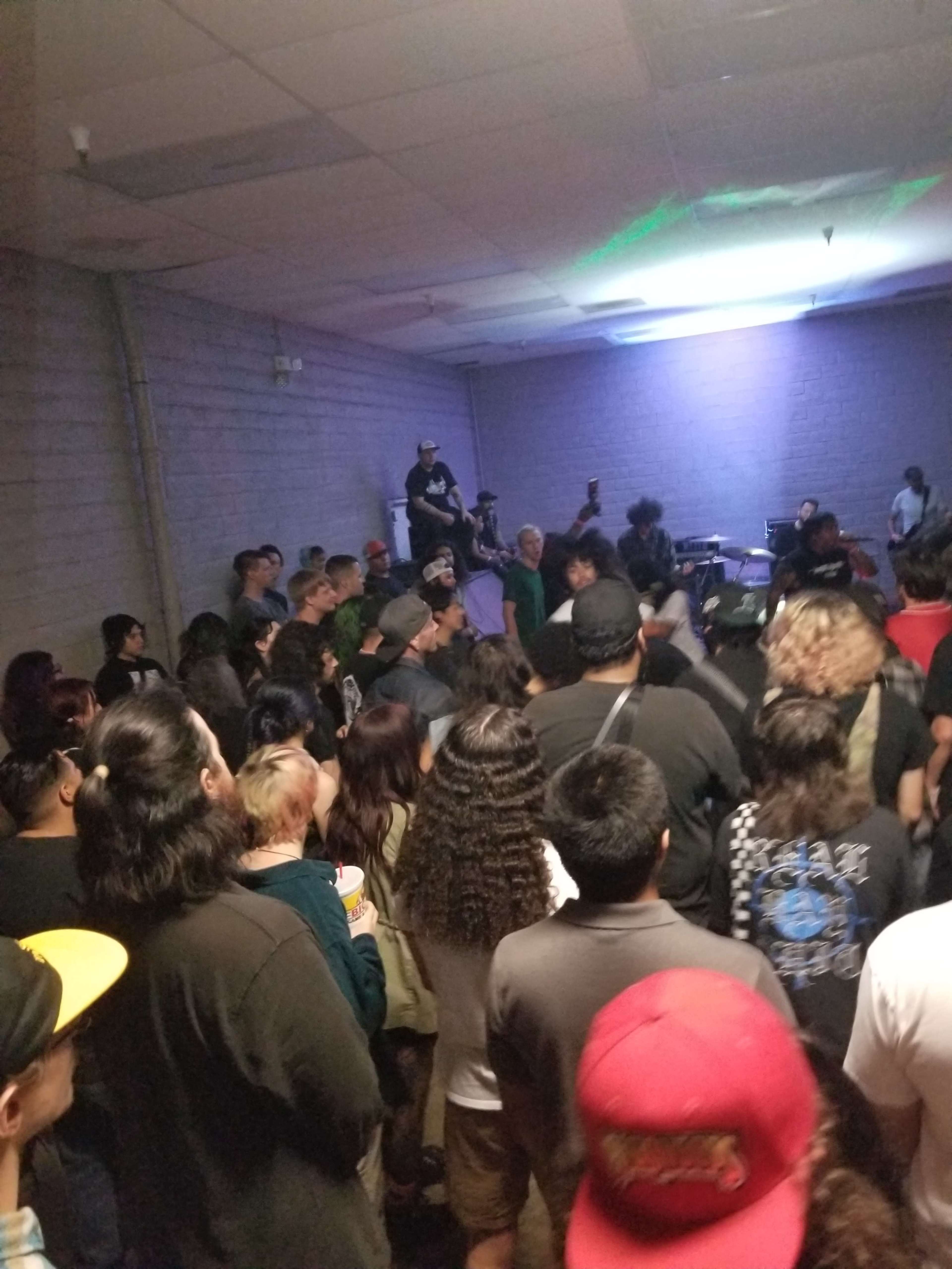 A crowd of people is gathered in a dimly lit room, watching a live band perform on stage.
