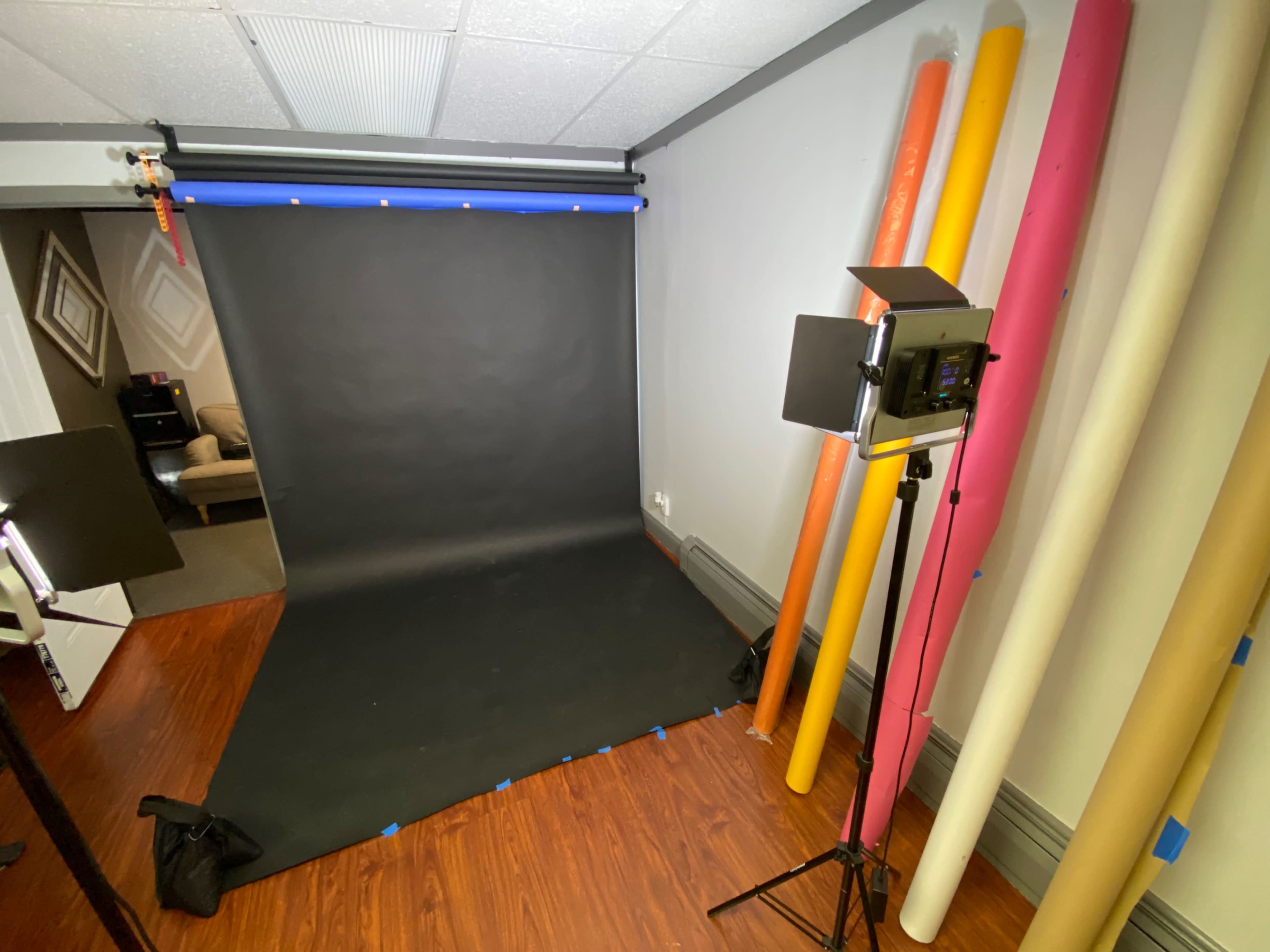 A photography studio setup with a black backdrop, lit by a light source, and various colored rolls of backdrop paper along the wall.